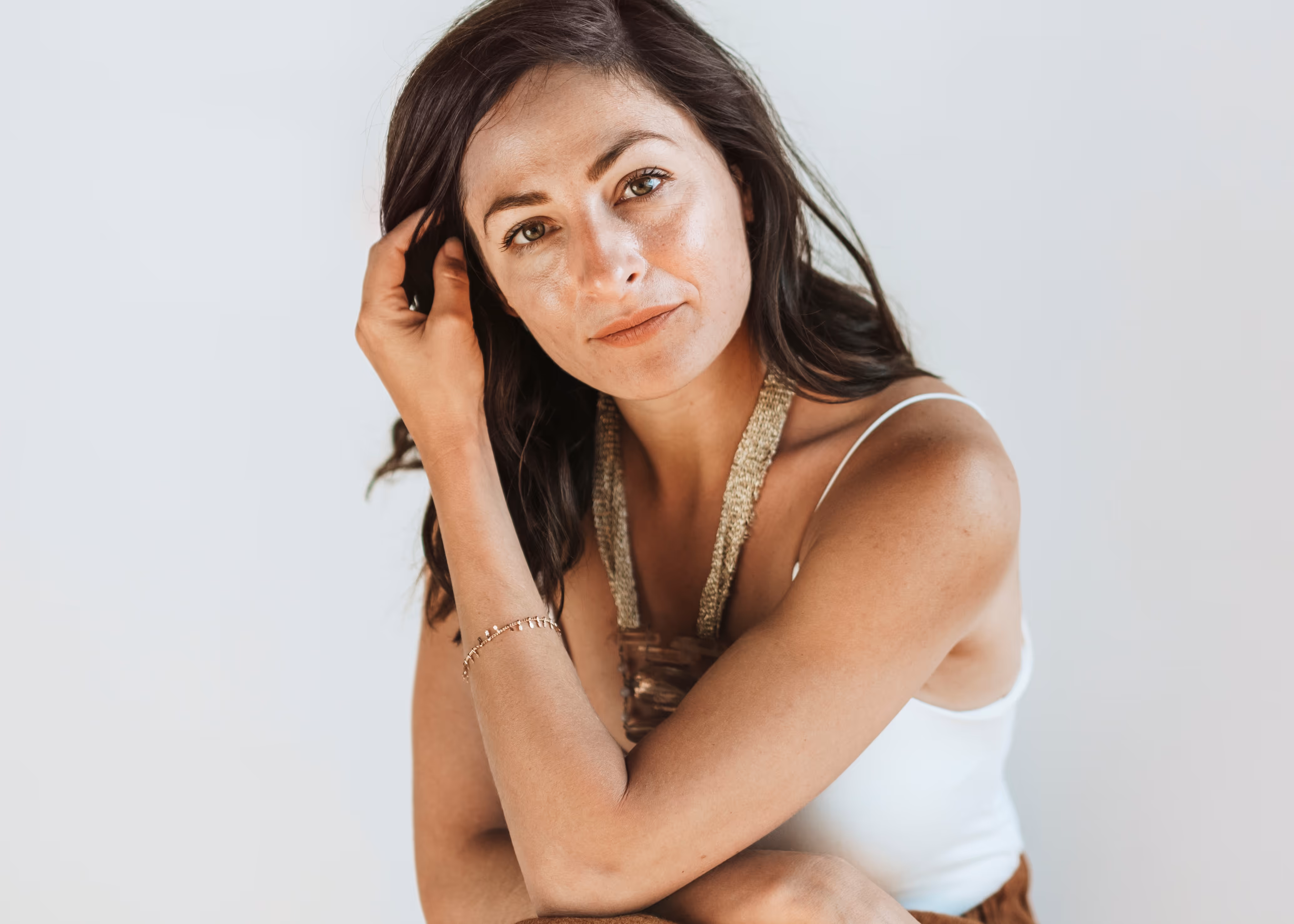 Woman with long dark hair wearing a white top and statement necklace looking thoughtfully at the camera.