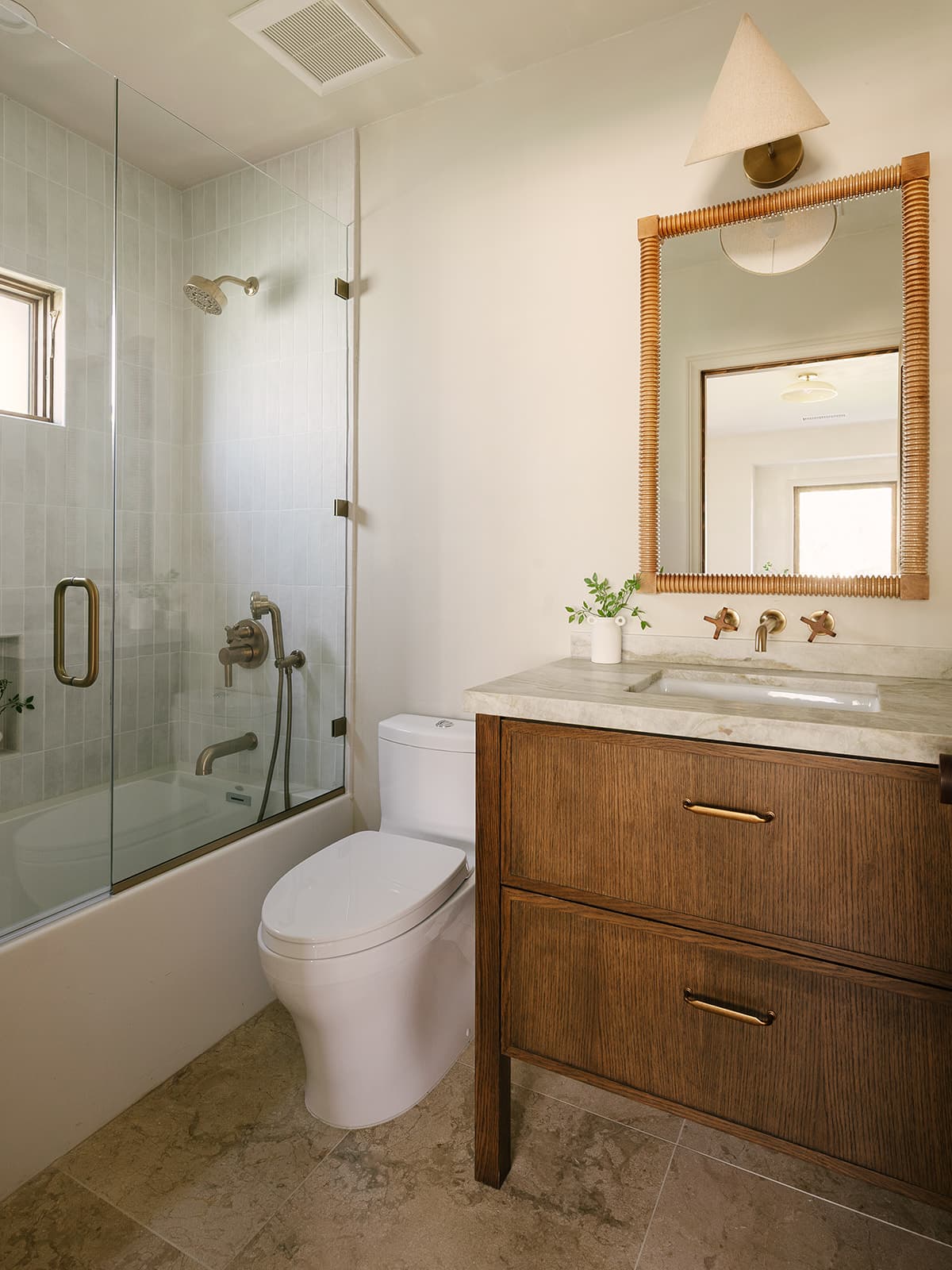 Modern bathroom with a white toilet, glass-enclosed bathtub with shower, and wood vanity with marble countertop and square mirror.