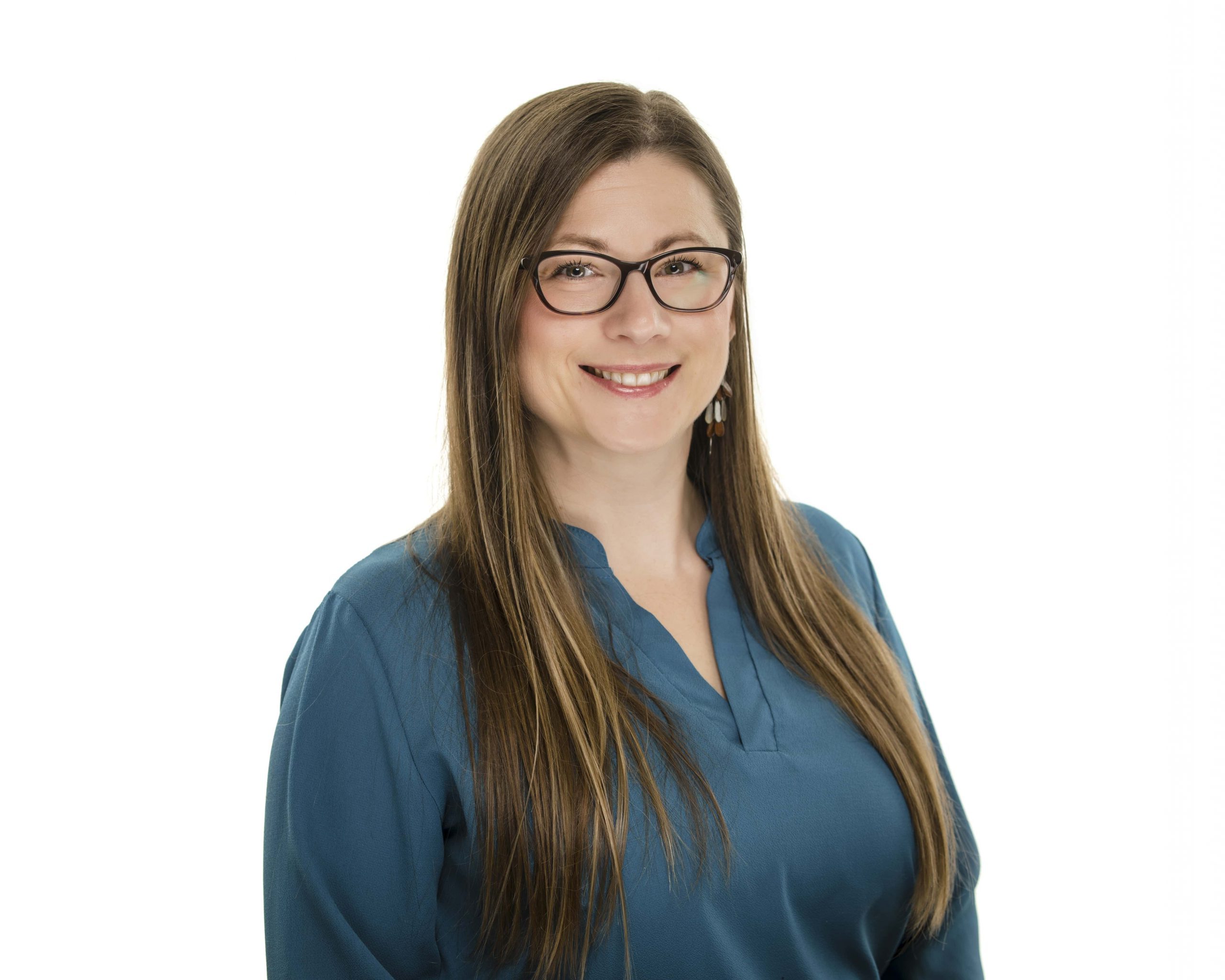 Smiling woman with long brown hair wearing glasses and a blue blouse against a white background.