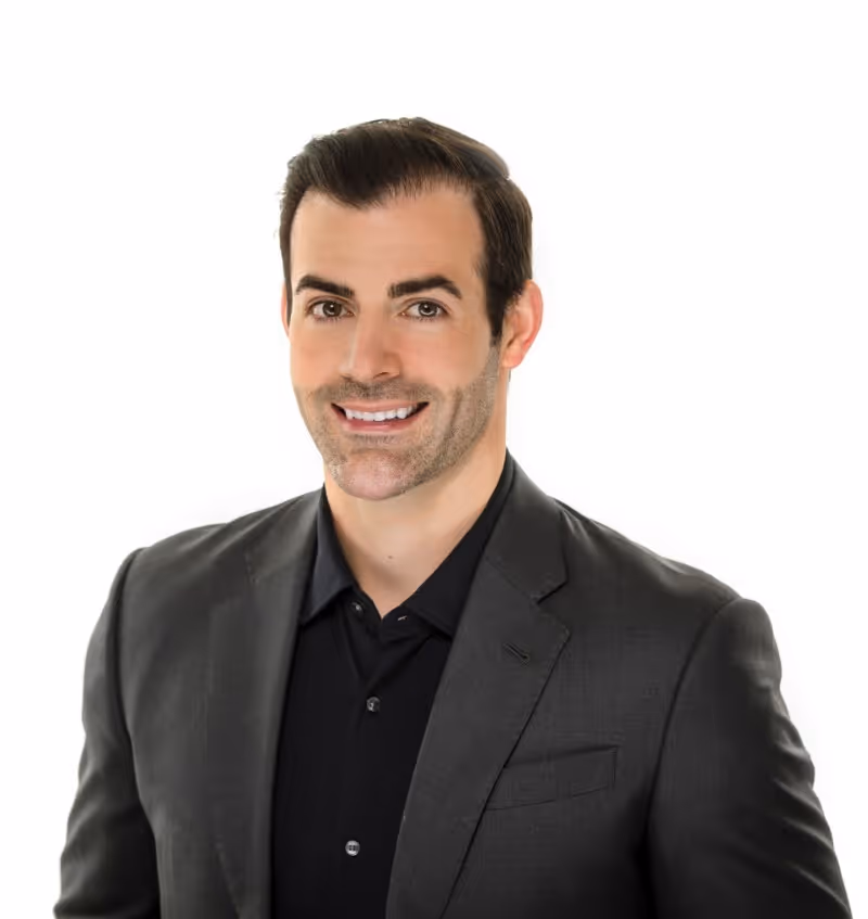Smiling woman with long brown hair wearing glasses and a blue blouse against a white background.