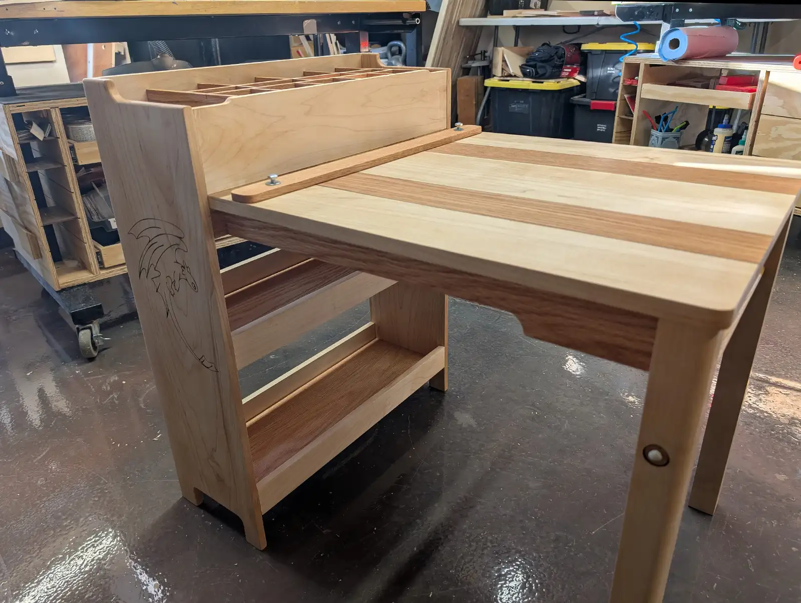 Custom handcrafted art table in a woodworking shop with built-in storage, paper roll holder, and detailed wood construction.