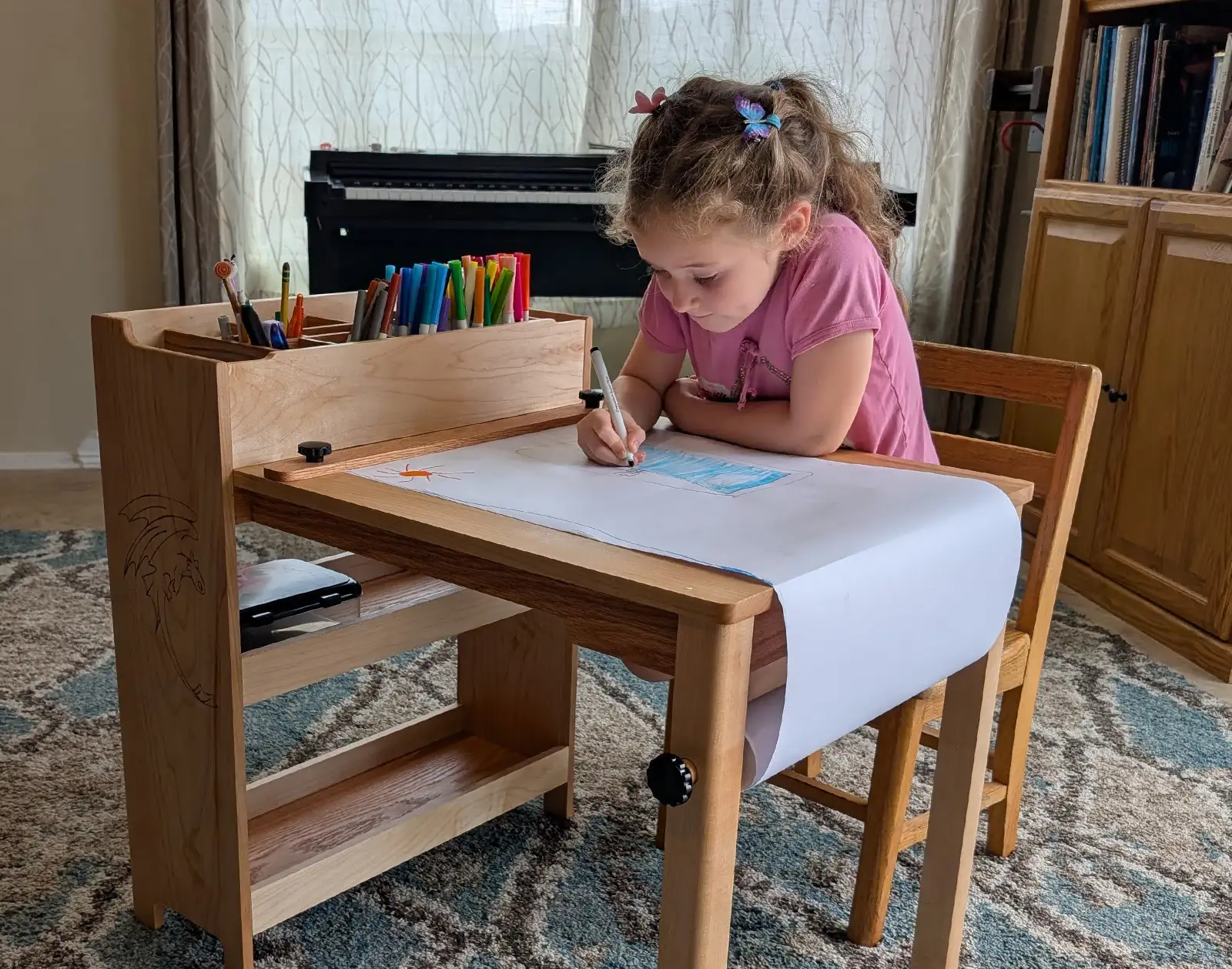 Child drawing at a custom wooden art table with paper roll, built-in marker storage, and handcrafted supply organizer.