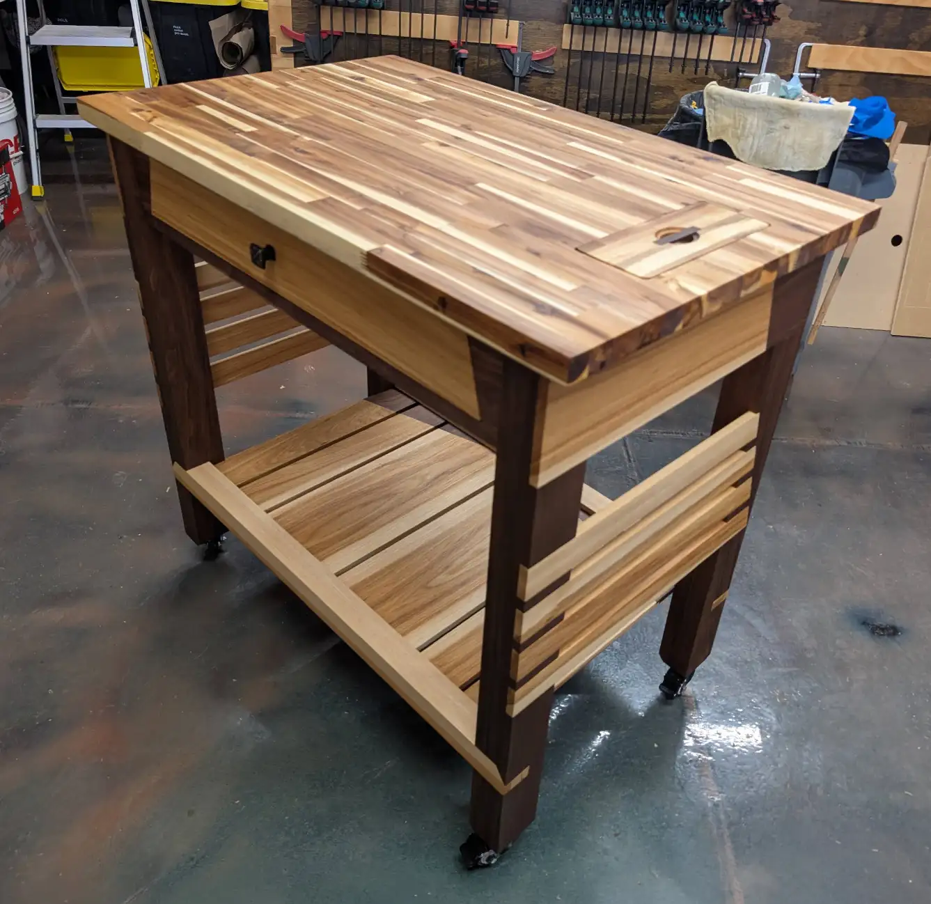 Rolling kitchen prep island with butcher block top, built-in drawer, lower storage shelf, and contrasting hardwood details.