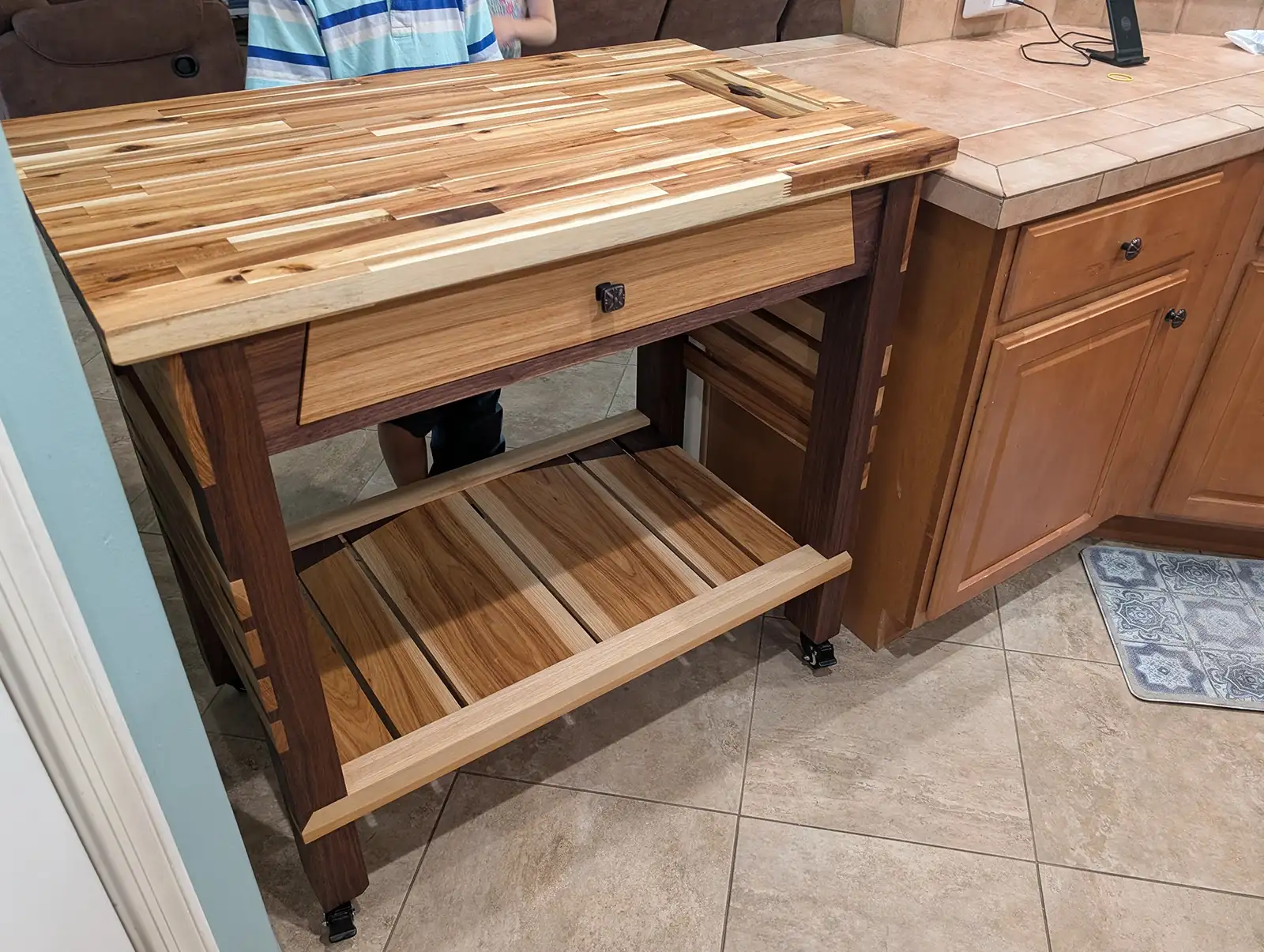Custom rolling kitchen island with butcher block cutting board top, storage drawer, open lower shelf, and locking caster wheels.