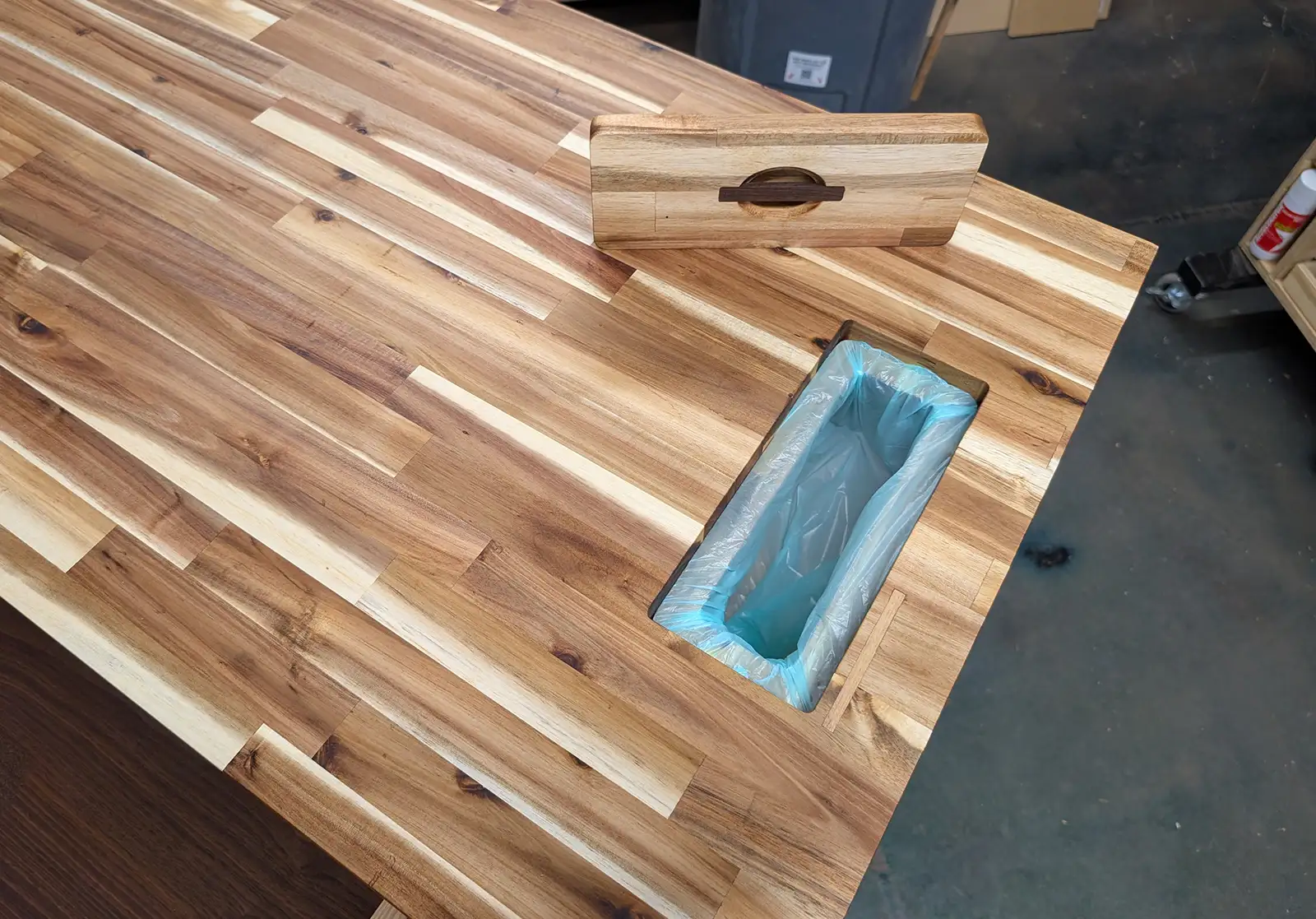 Built-in scrap chute on a wooden kitchen island with full cutting board surface and removable lid for easy meal prep cleanup.