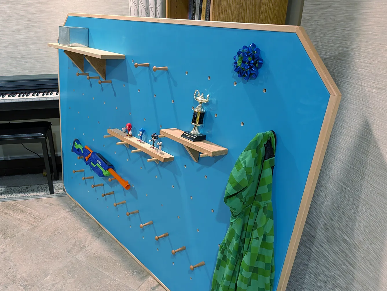 Large modular children’s pegboard with adjustable wooden pegs, shelves, toy display, and hanging storage for a playroom or bedroom.