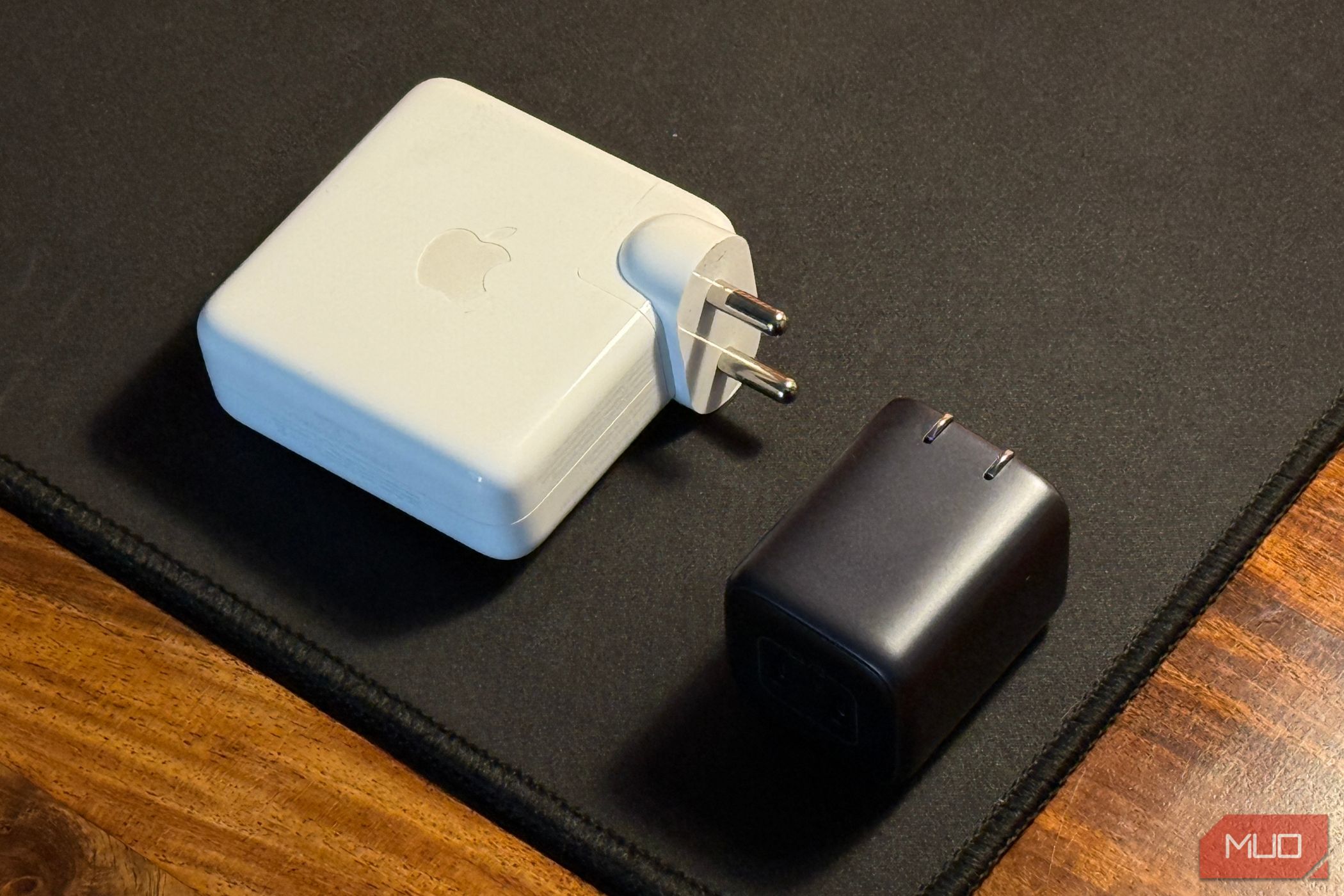 A compact charger next to a larger MacBook charger on a table.