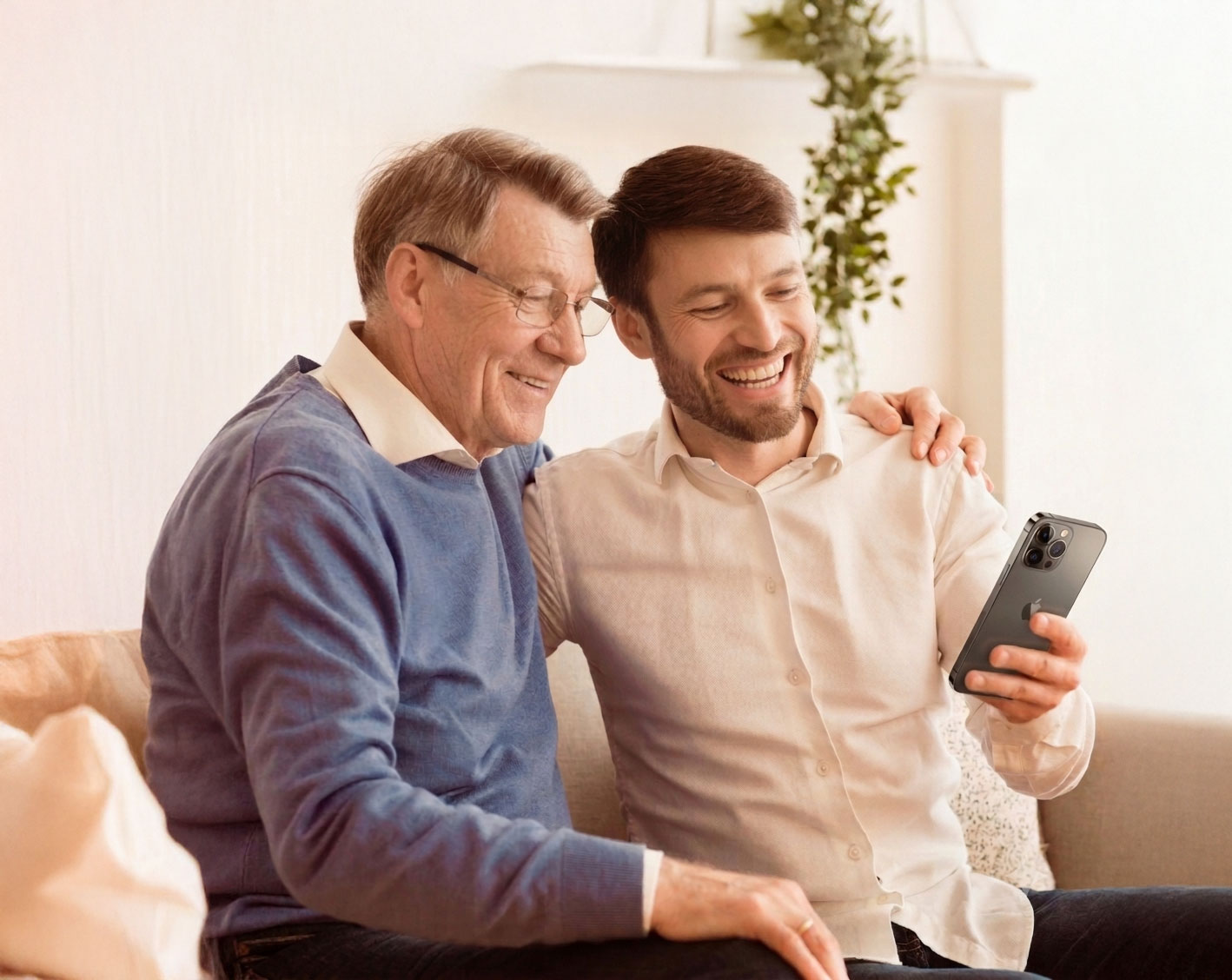 Älterer Mann und jüngerer Mann lachen, während sie auf einem Sofa ein Handy ansehen.