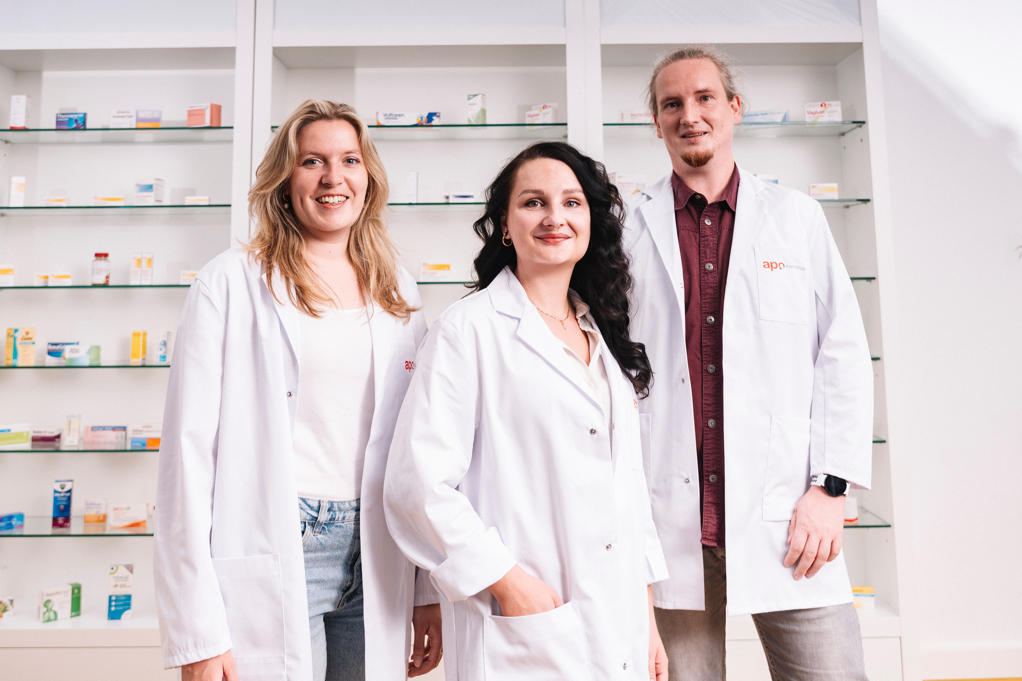 Drei Mitarbeitende des apodiscounter-Apothekenteams in weißen Kitteln vor einem Medikamentenregal – die Apotheke hinter MYA