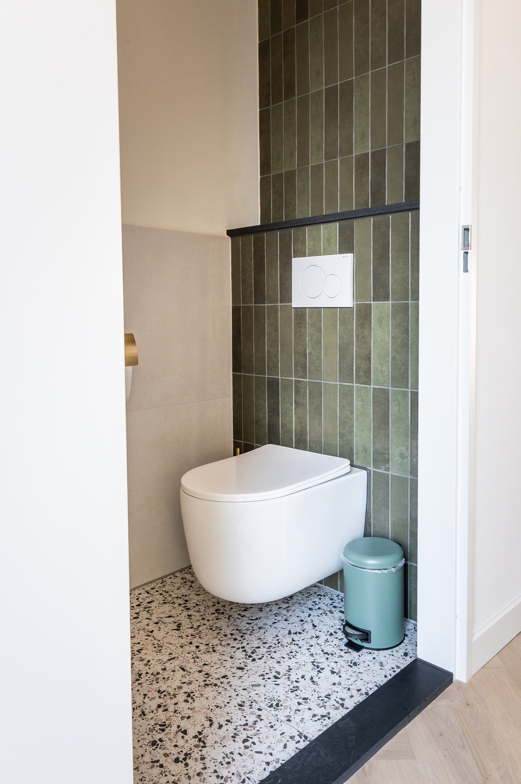 Doorkijk vanuit de gang naar een toiletruimte met donkergroene verticale tegels en terrazzovloer