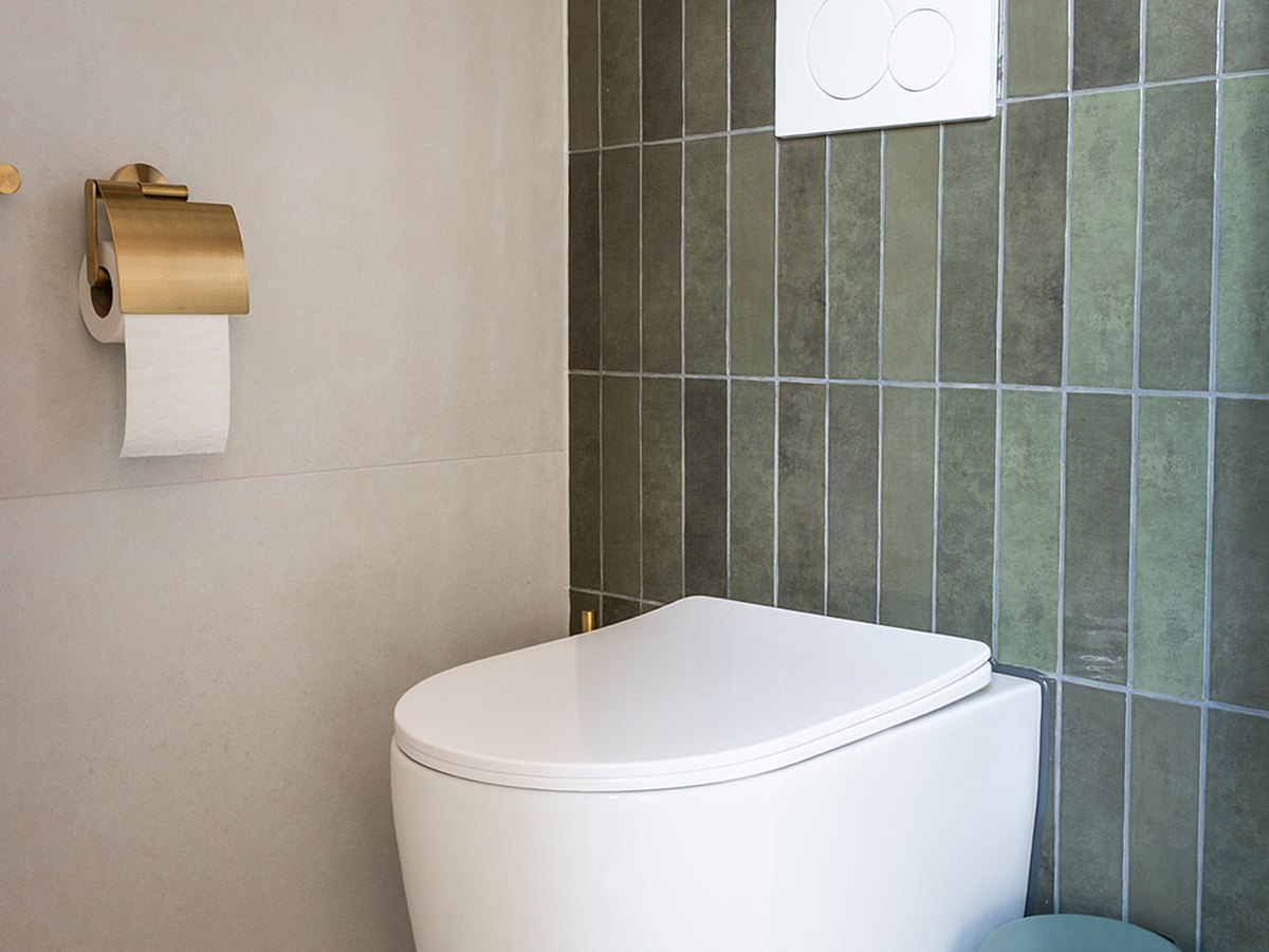 Toiletruimte met wit wandcloset tegen groene verticale tegels en een terrazzovloer