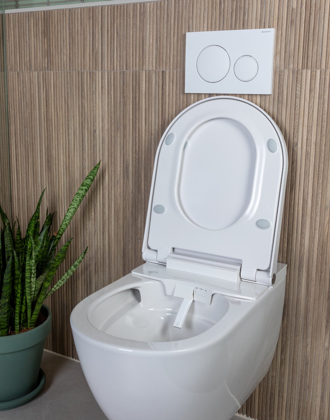 Douche-wc met geopend deksel tegen een houtlook wand, met de sproeier zichtbaar