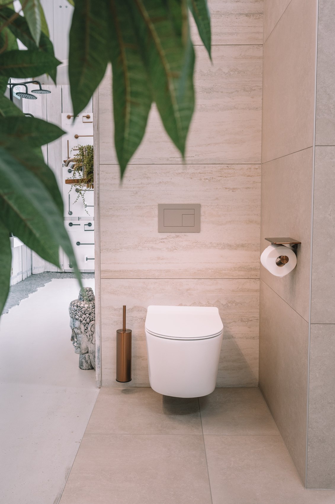 Wit wandcloset tegen travertijnlook tegels, met een grote groene plant