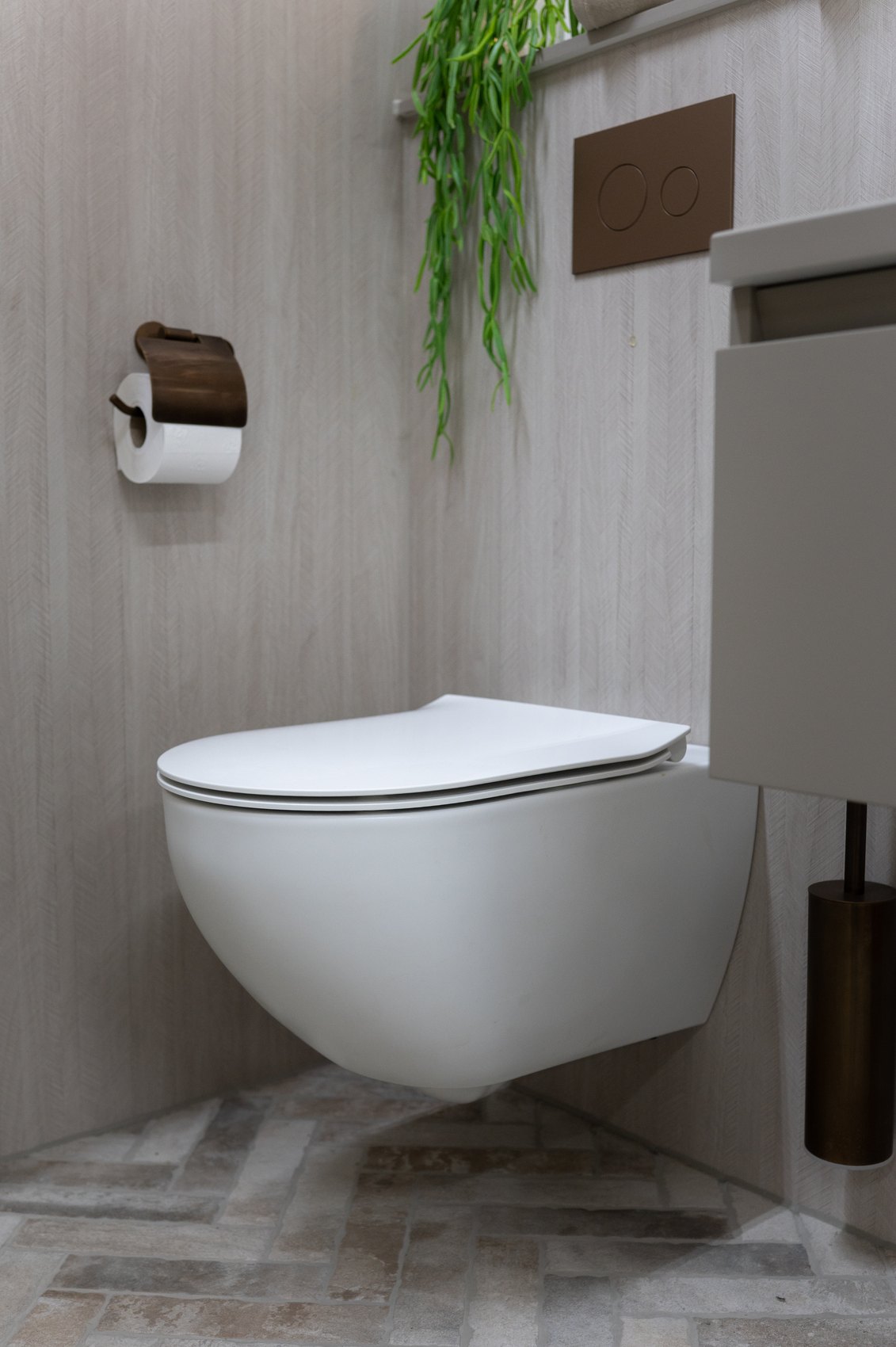 Wit wandcloset tegen een houtlook wand, met een bronzen toiletrolhouder en toiletborstel