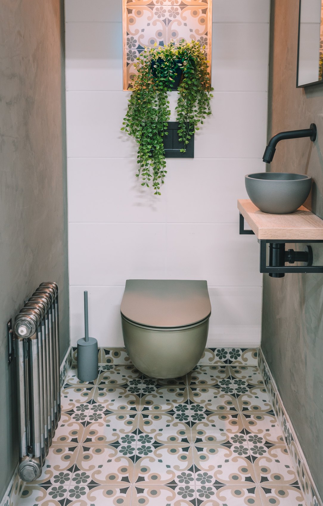 Complete toiletruimte met een olijfgroen wandcloset, patroontegelvloer, houten plank met stenen fonteintje en een hangplant