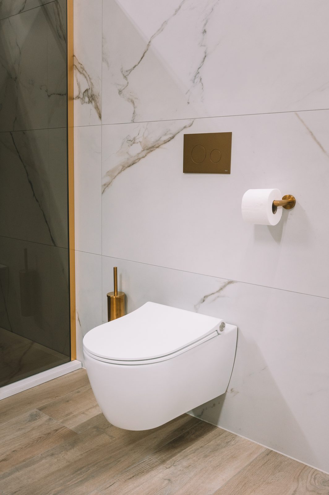 Wit wandcloset tegen marmerlook tegels met een gouden toiletrolhouder