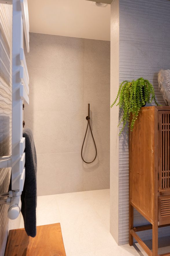 Doucheruimte met handdoekradiator, bronzen doucheslang en een houten kastje met plant