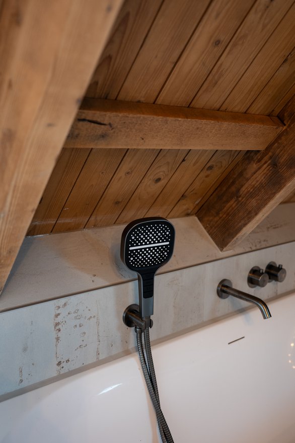Handdouche aan de wand boven de rand van een bad, met een houten plafond en balken erboven.