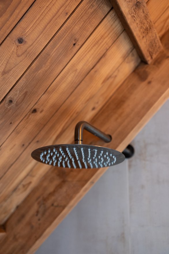 Ronde regendouchekop aan een wand van verweerde houten planken.