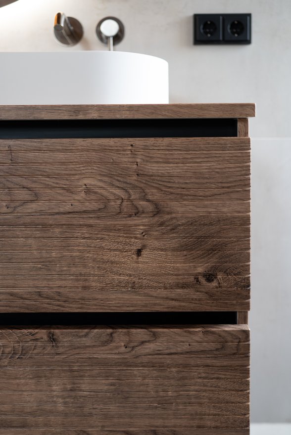 Houten ladefront van een wastafelmeubel met een witte waskom op het blad erboven.