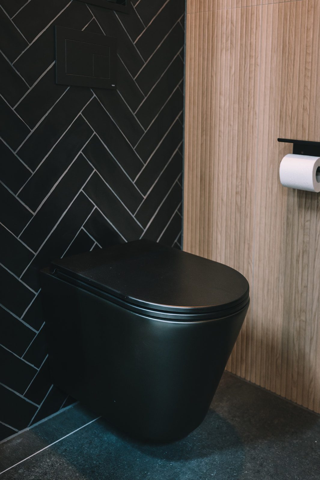 Toiletruimte met zwarte visgraattegels en houtlook wand