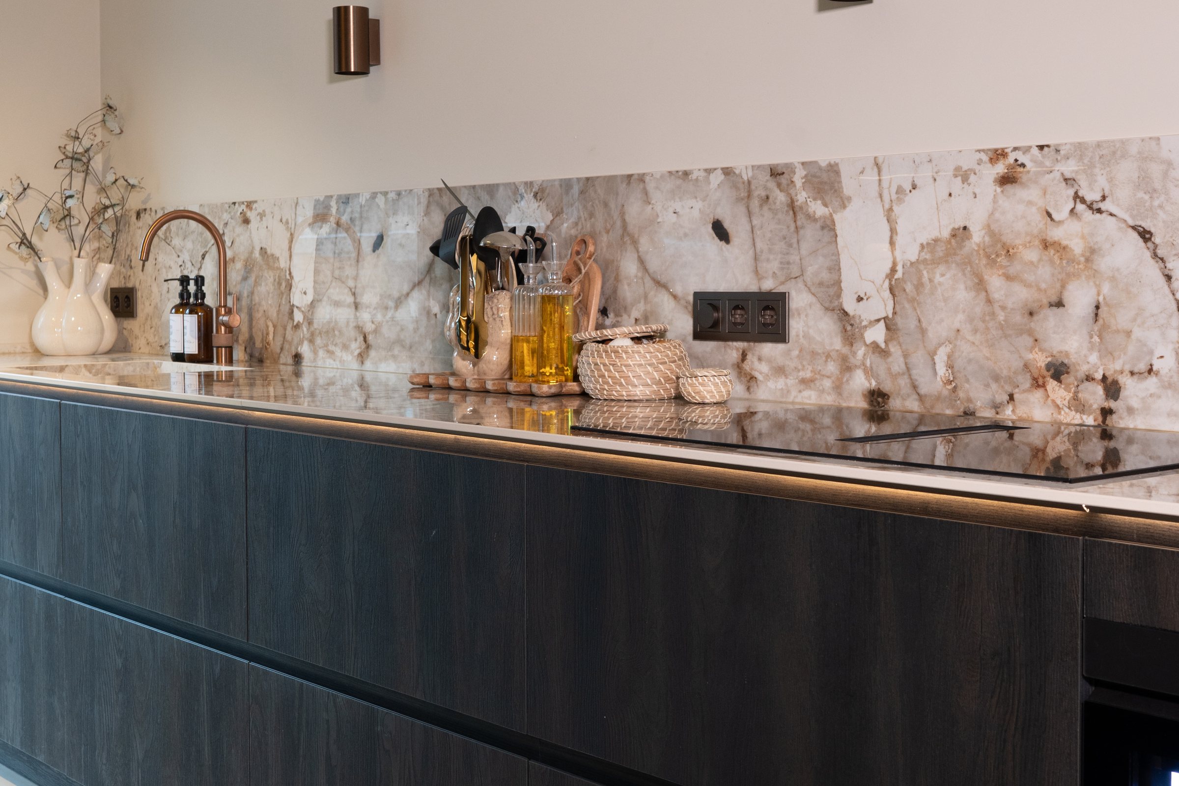 Greeploze keukenwand in donker hout met een marmerlook achterwand en een inductiekookplaat.