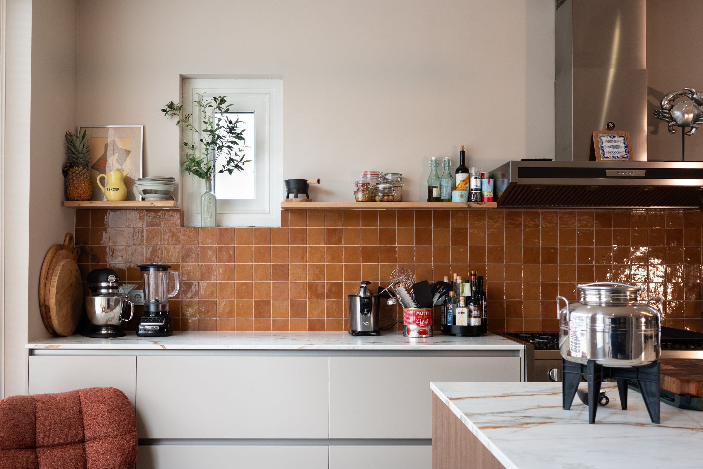 De terracotta tegelwand langs het aanrecht, met een open plank erboven en de koffiehoek eronder.