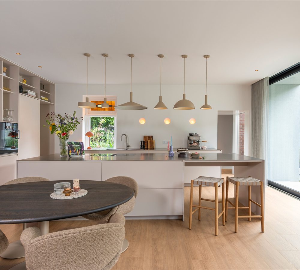 Open keuken met kookeiland en een lichte plankenvloer die doorloopt naar de tuindeuren