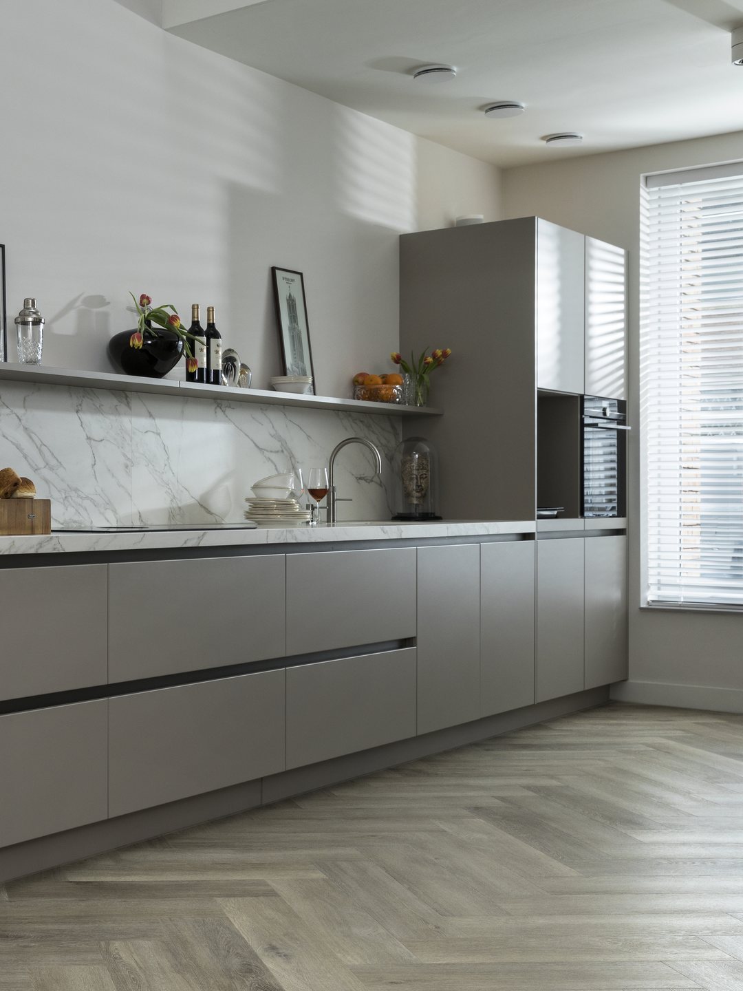 Grijze keukenwand met een marmerlook achterwand en daarvoor een lichte visgraatvloer