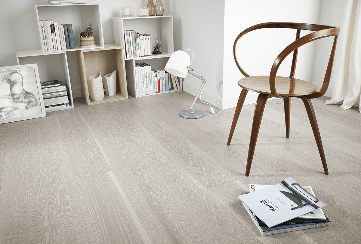 Hoek van een woonkamer met een lichte plankenvloer met zichtbare nerf, een houten stoel en een bureaulamp