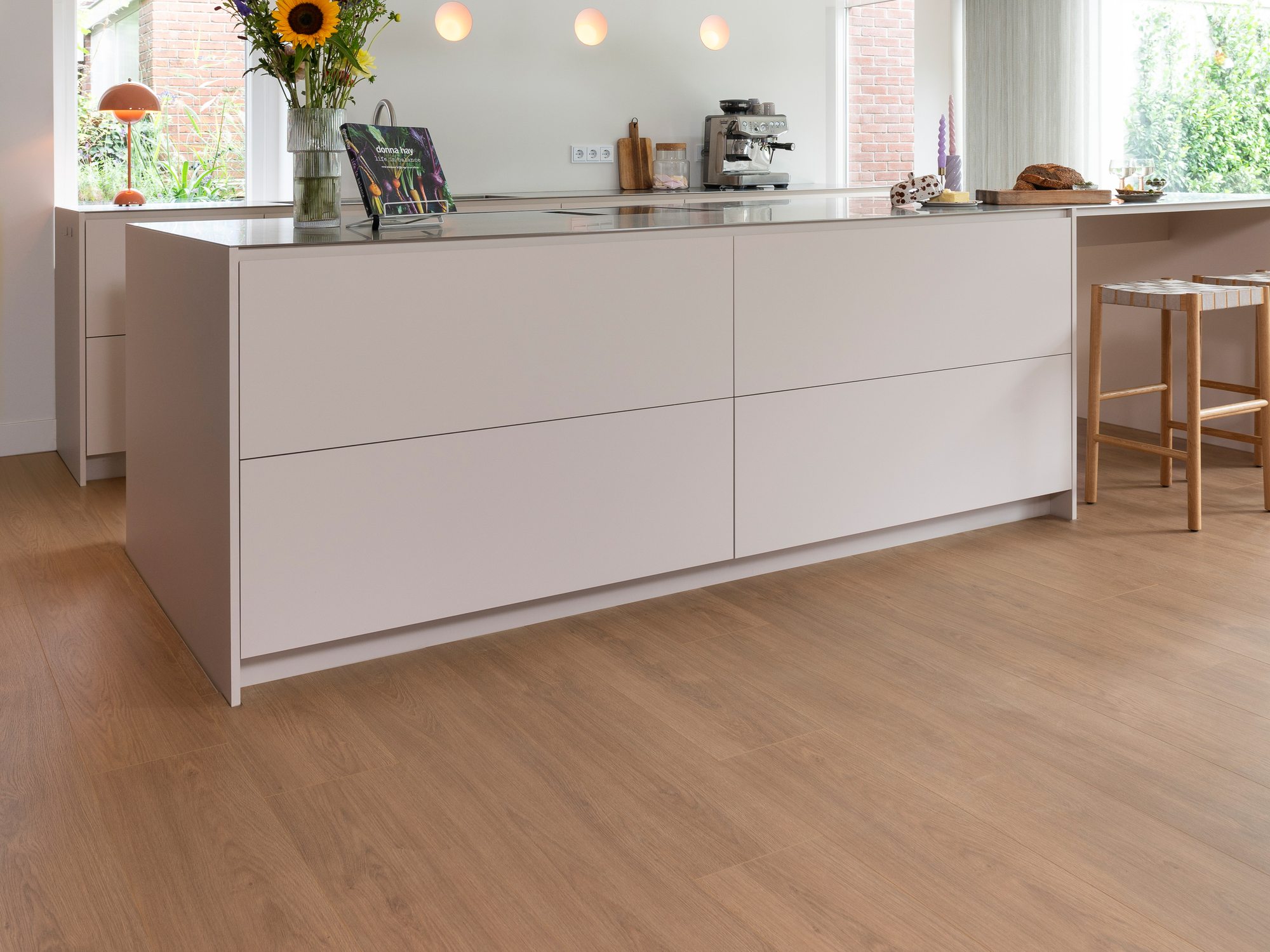 Open keuken met een licht kookeiland en een lichte plankenvloer die tot aan de tuinzijde doorloopt
