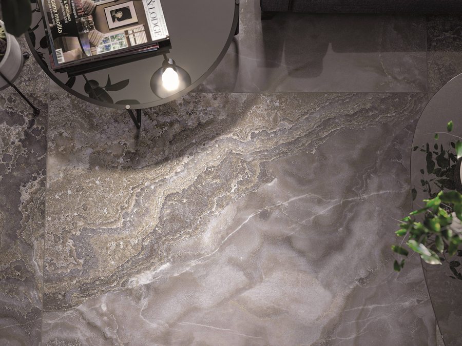 Detailopname van een vloer met grootformaat tegels in grijsbruine steenlook, met een bijzettafel en een plant