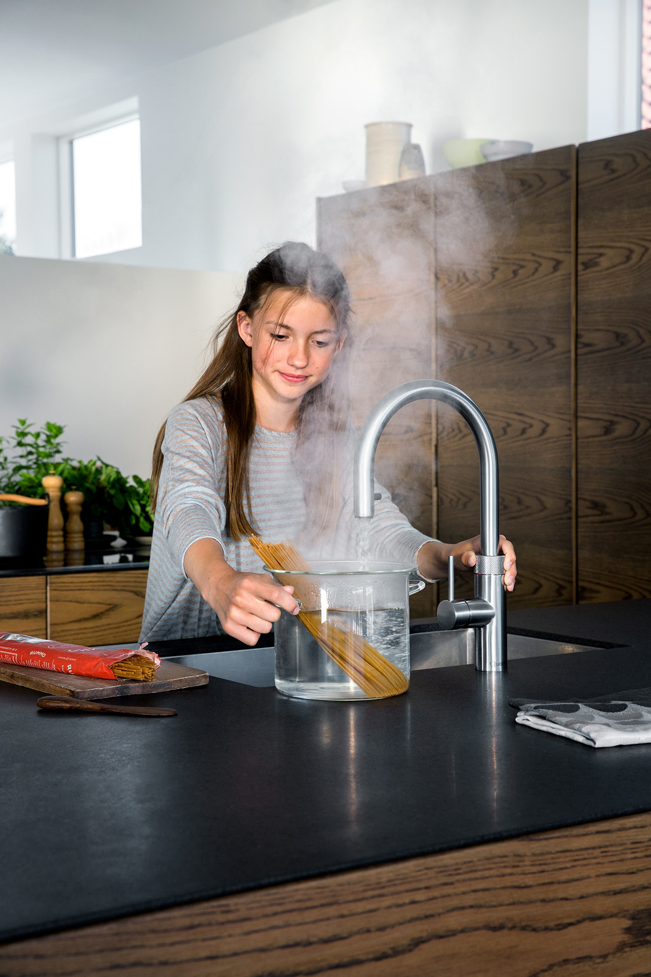 Meisje laat spaghetti in een pan dampend water glijden naast een kokendwaterkraan