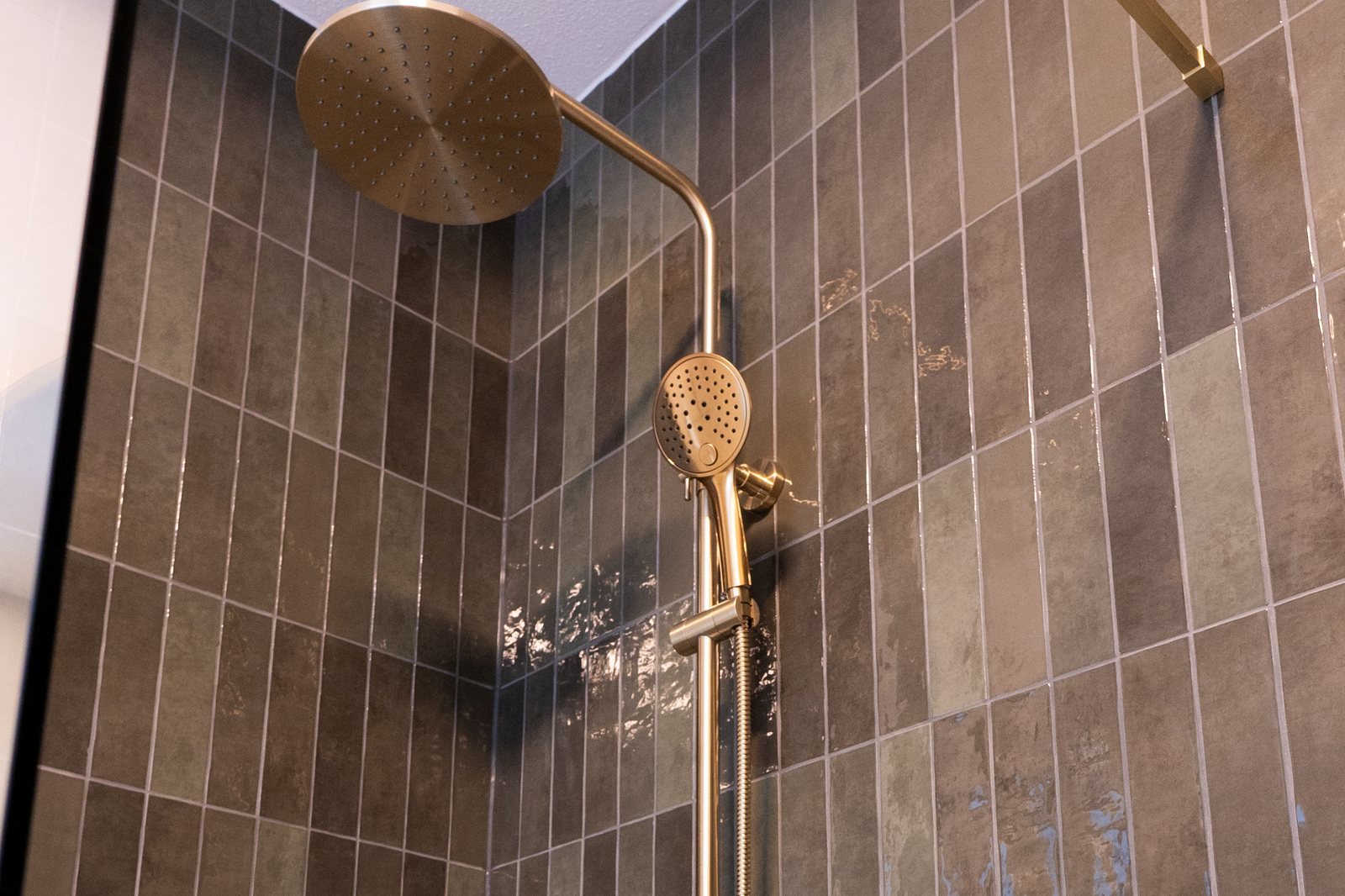 Messing regendouche en handdouche tegen glanzende bruingroene stroktegels