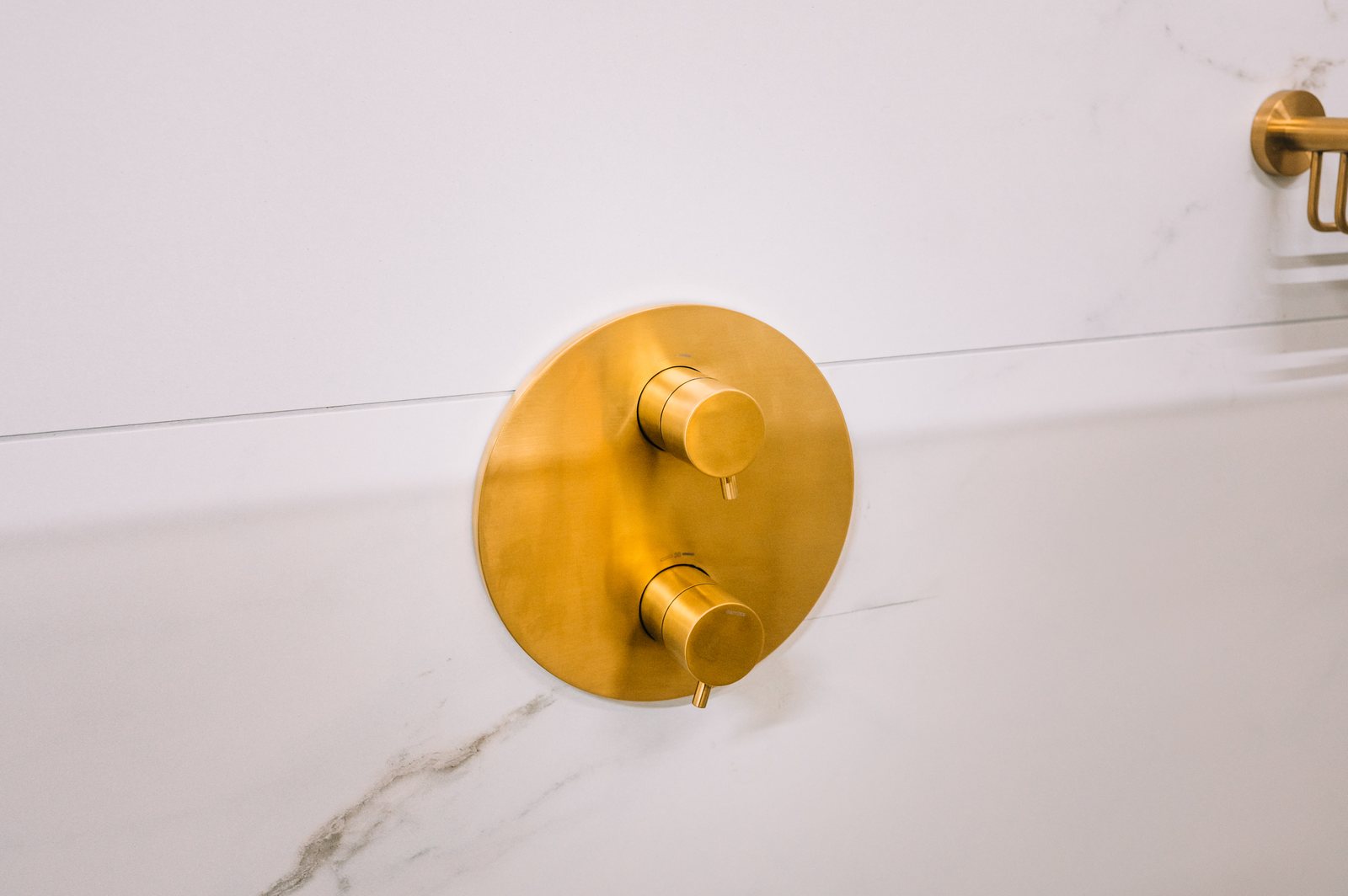 Gouden inbouwbediening voor de douche op een wand van witte marmerlook