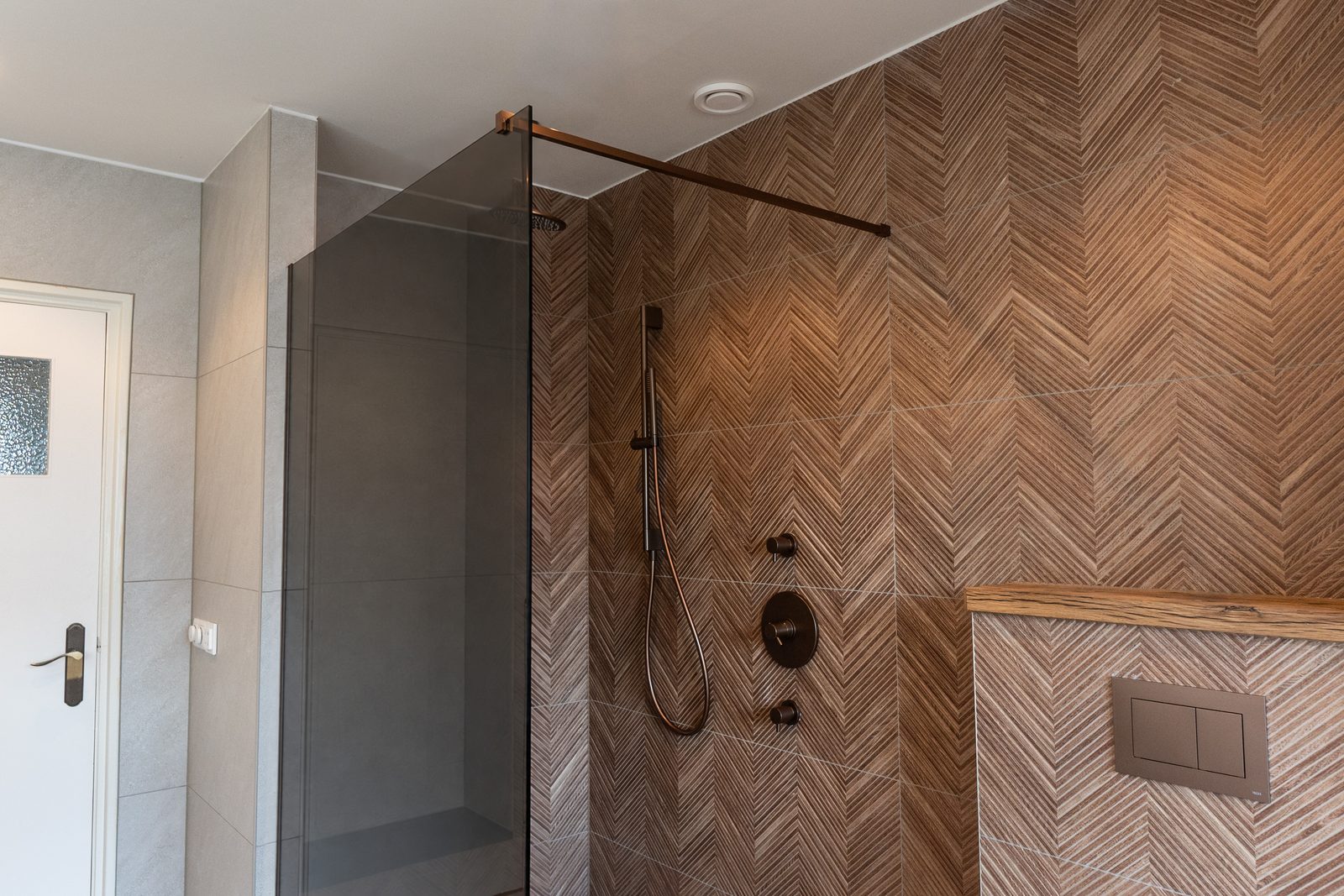 Douche met regendouche en handdouche tegen een wand in visgraat-houtlook, naast een rookglas douchewand