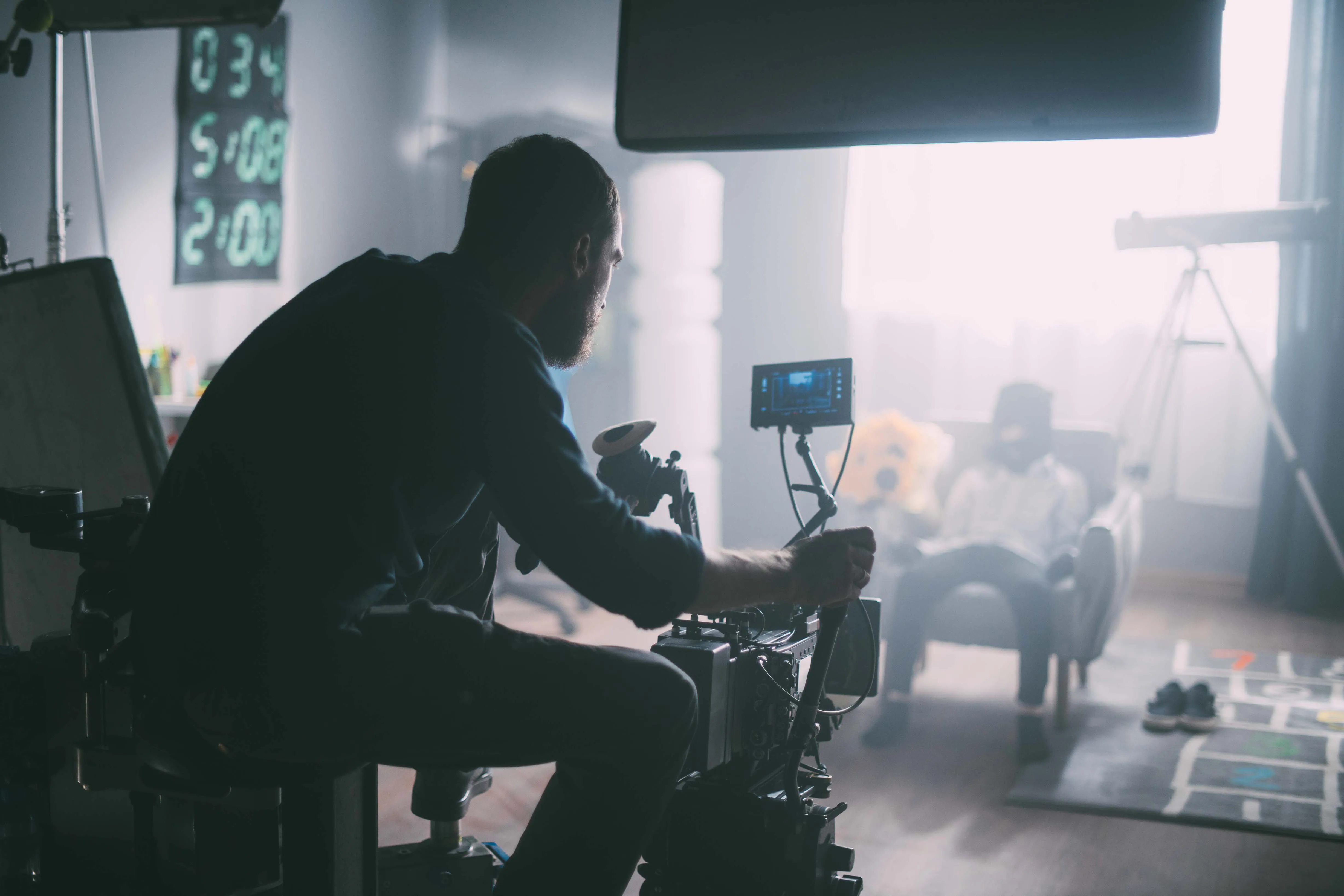 Making-Of Bild: Kameramann sitz hinter der Kamera und filmt einen Mann in einem Stuhl.