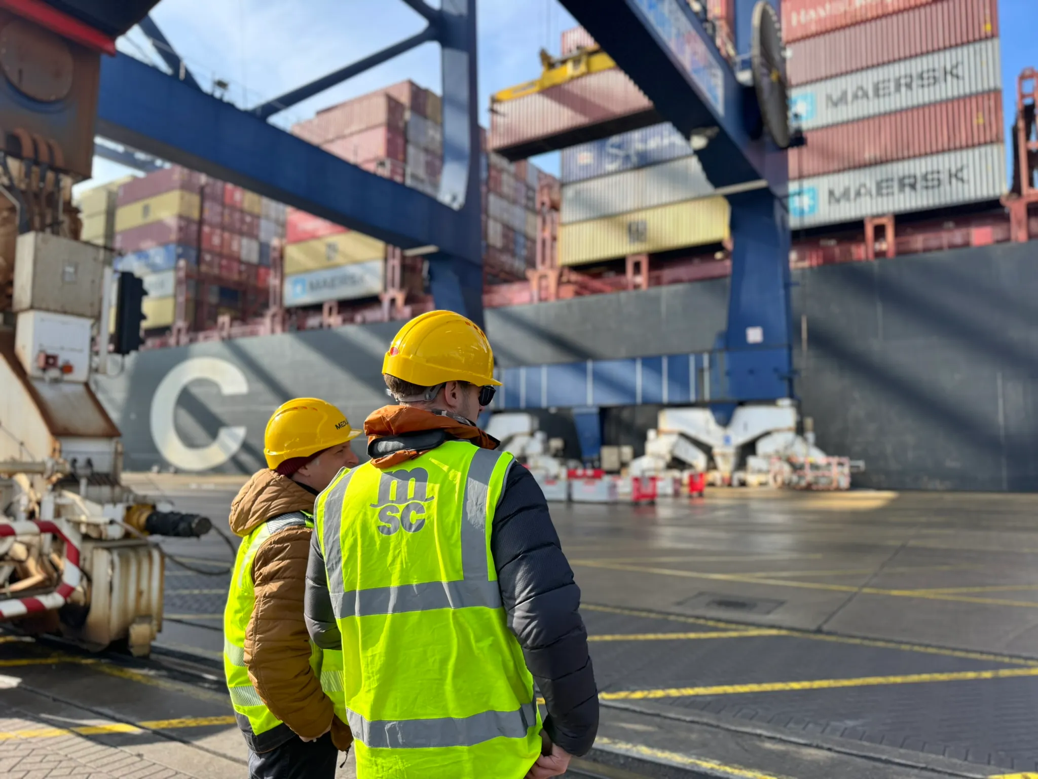 Making-Of Bild: zwei Personen stehen vor einem großen Containerschiff am Hafen