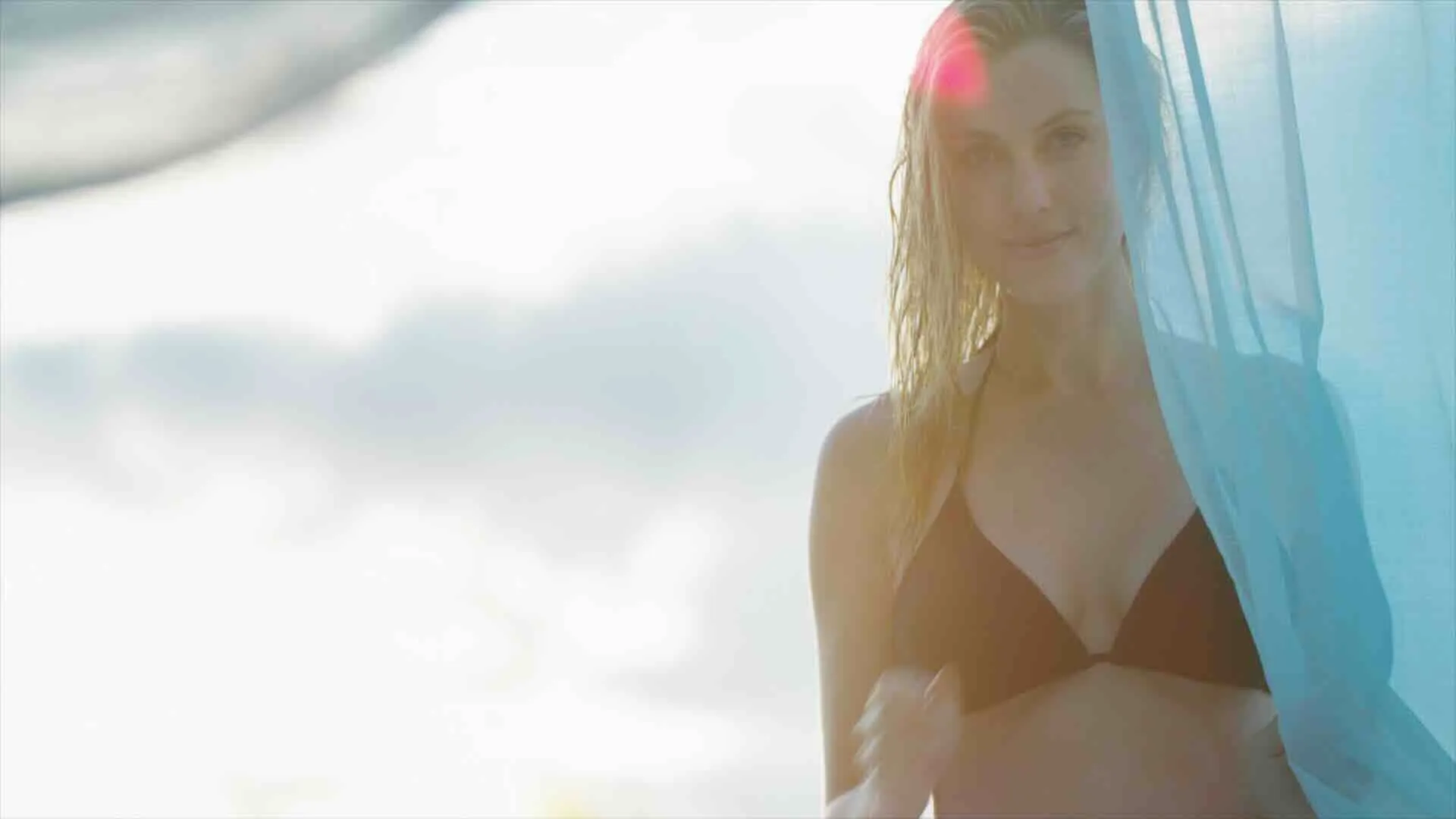 Still: ein Frau in Bikini schiebt einen Vorhang zur Seite.