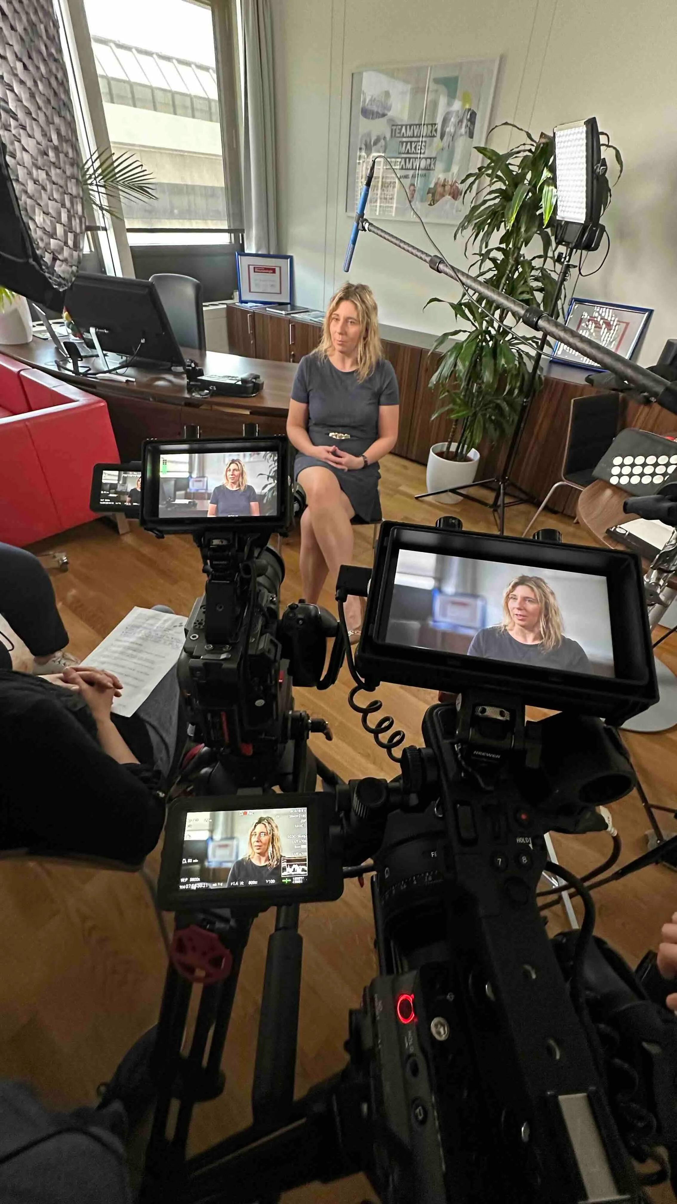 Frau sitzt im Büro für ein Interview, umgeben von Kameras, Mikrofon und Beleuchtungsausrüstung.