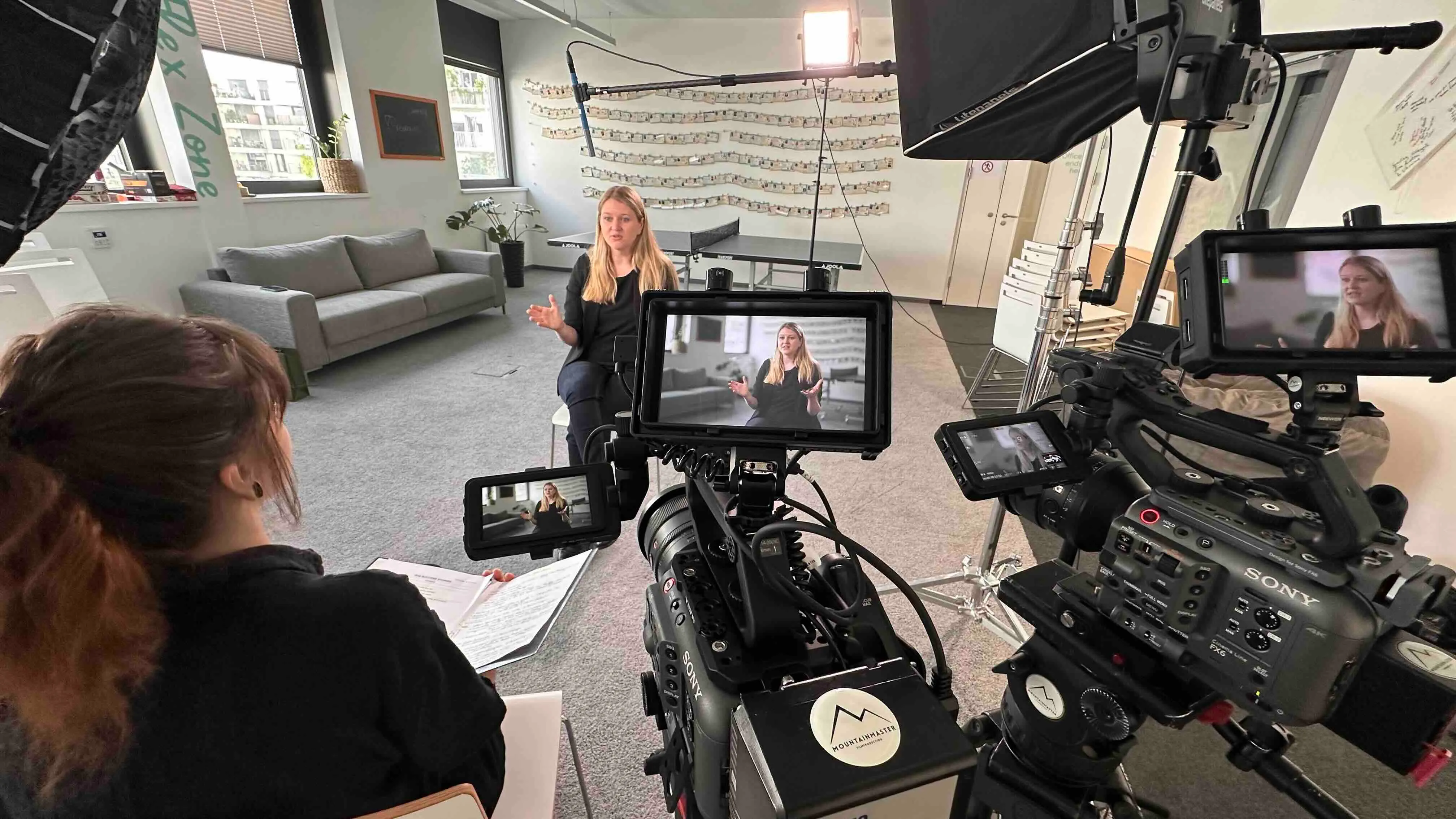 Dreharbeiten in einem Büro mit einer Frau, die auf einem Stuhl sitzt und vor mehreren Kameras spricht.