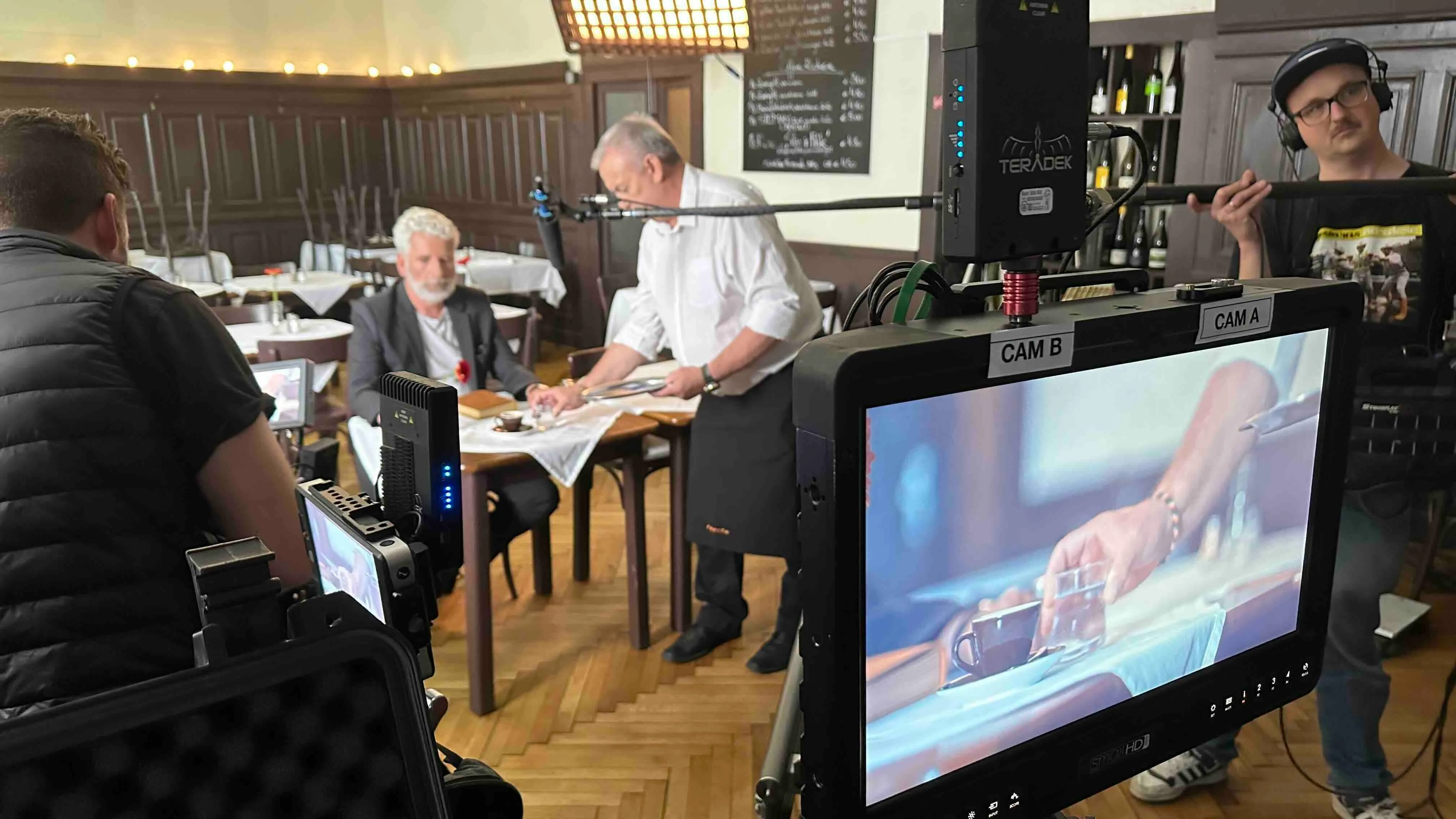 Dreharbeiten in einem Restaurant mit Kameramann, Tontechniker, Kellner und einem älteren Mann am Tisch.