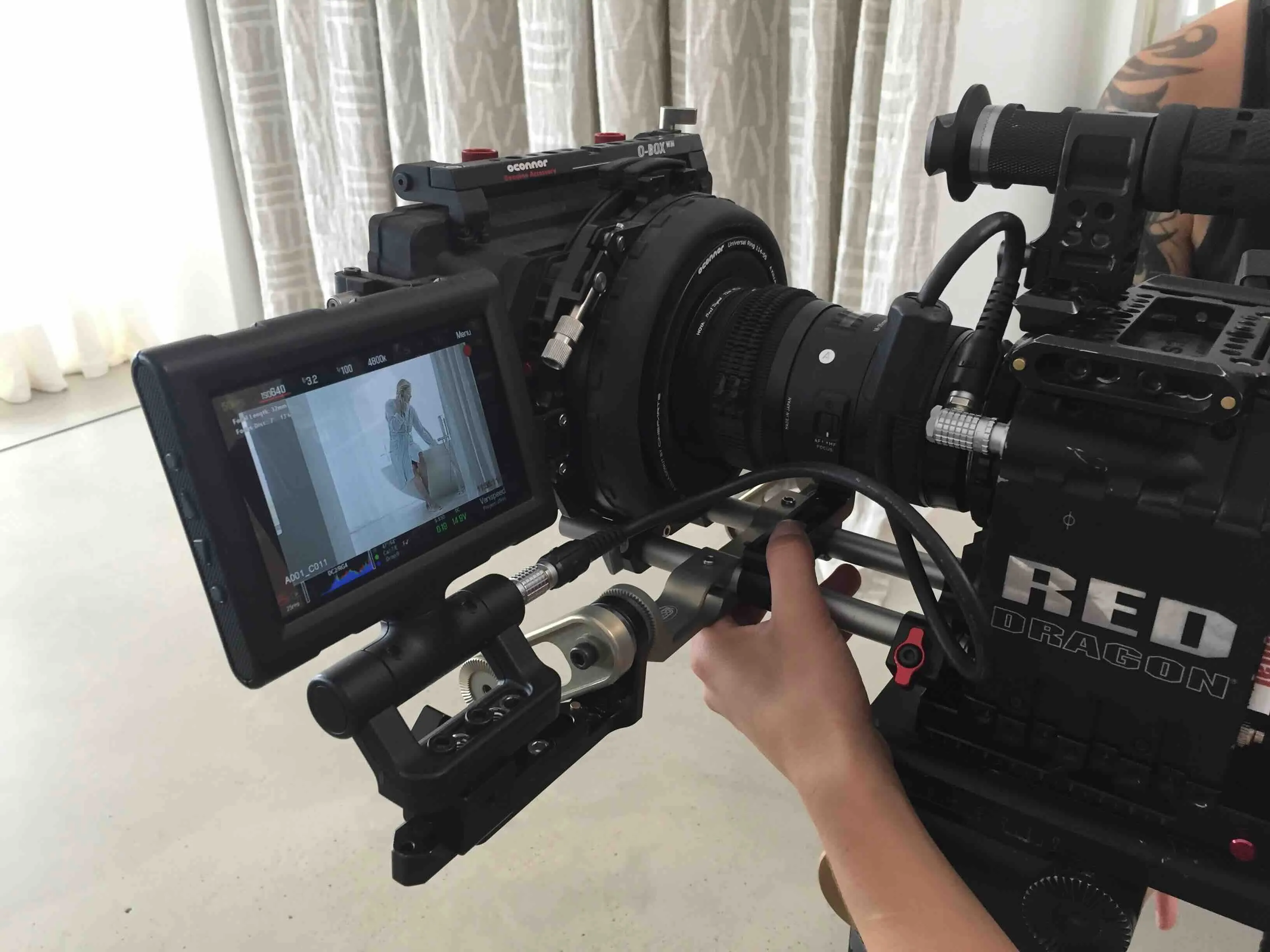 Hand justiert eine RED Dragon Profi-Filmkamera mit Monitor, der eine Frau in hellem Raum zeigt.