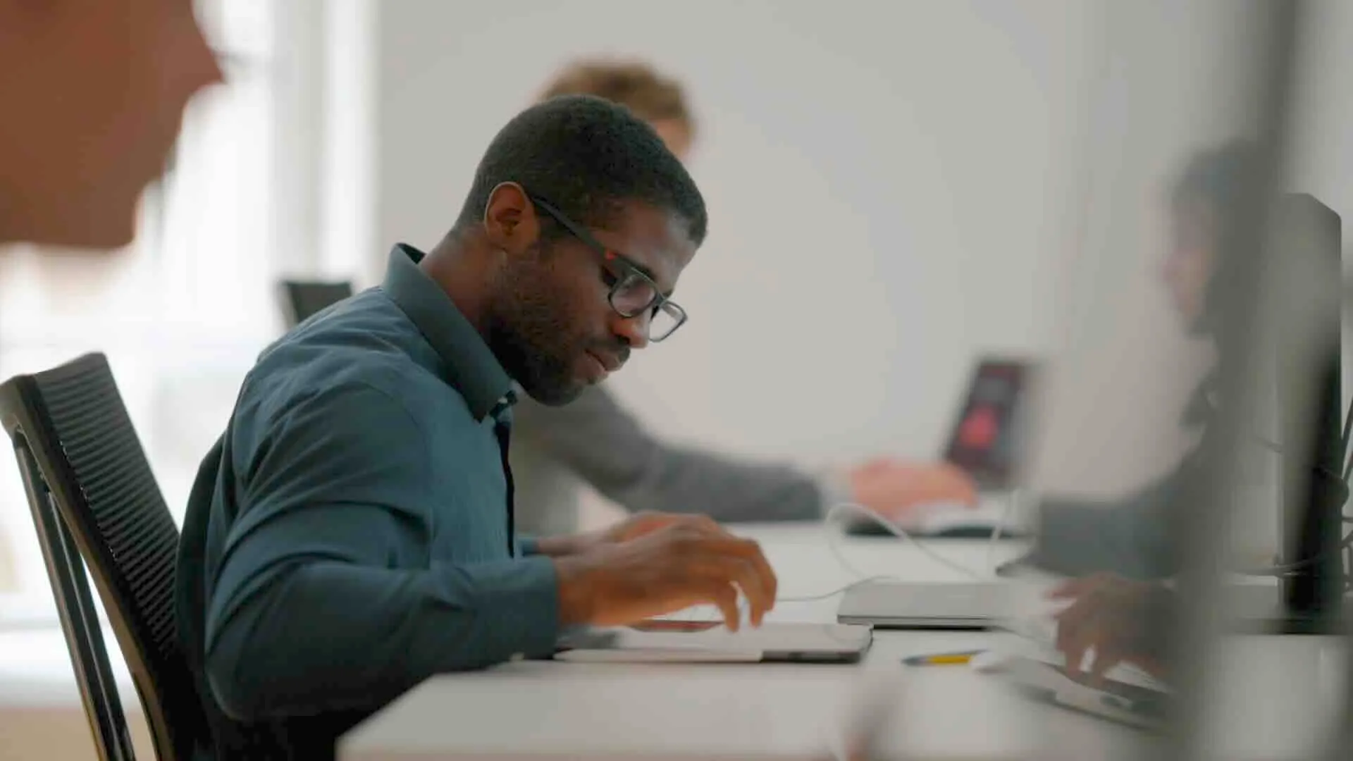 Mann mit Brille und blauem Hemd arbeitet konzentriert an einem Tablet an einem Schreibtisch in einem Büro.