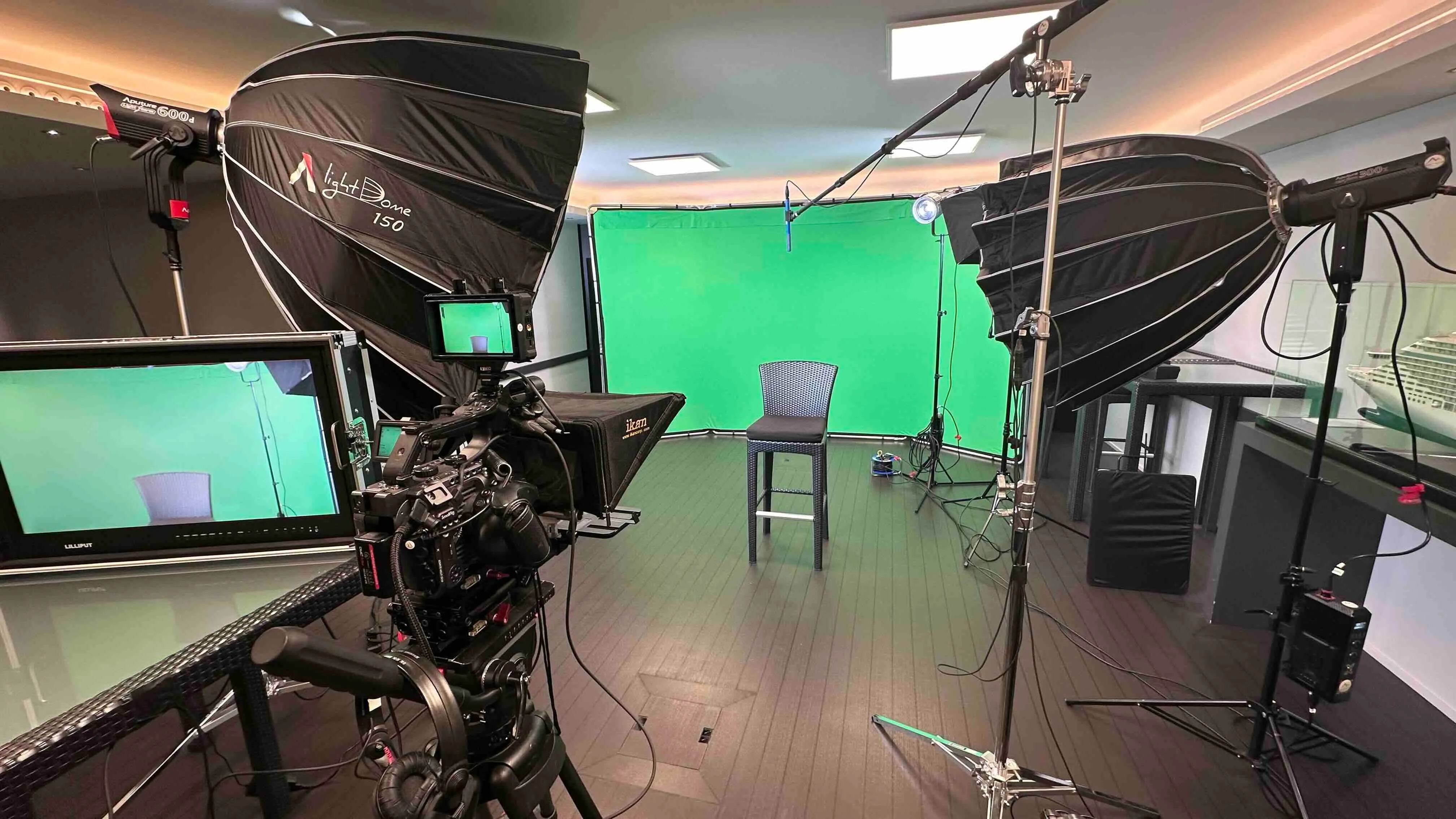 Innenaufnahme eines professionellen Fotostudios mit grünem Hintergrund, Kamera, Beleuchtungsausrüstung und einem Stuhl in der Mitte.