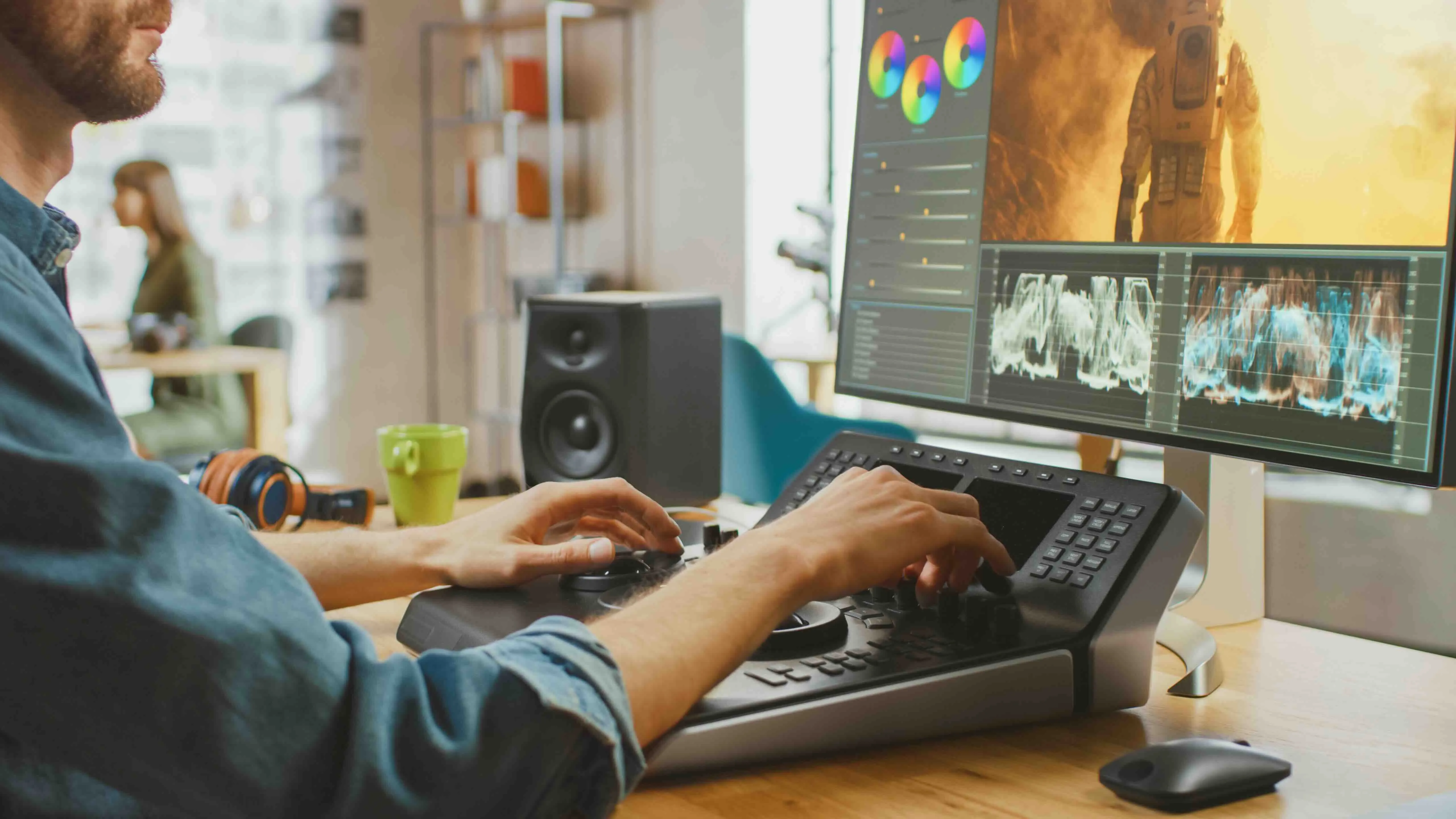 Person bearbeitet Video auf einem Farbkorrektur-Controller mit Monitor, der Farbräder und Wellenformen zeigt.