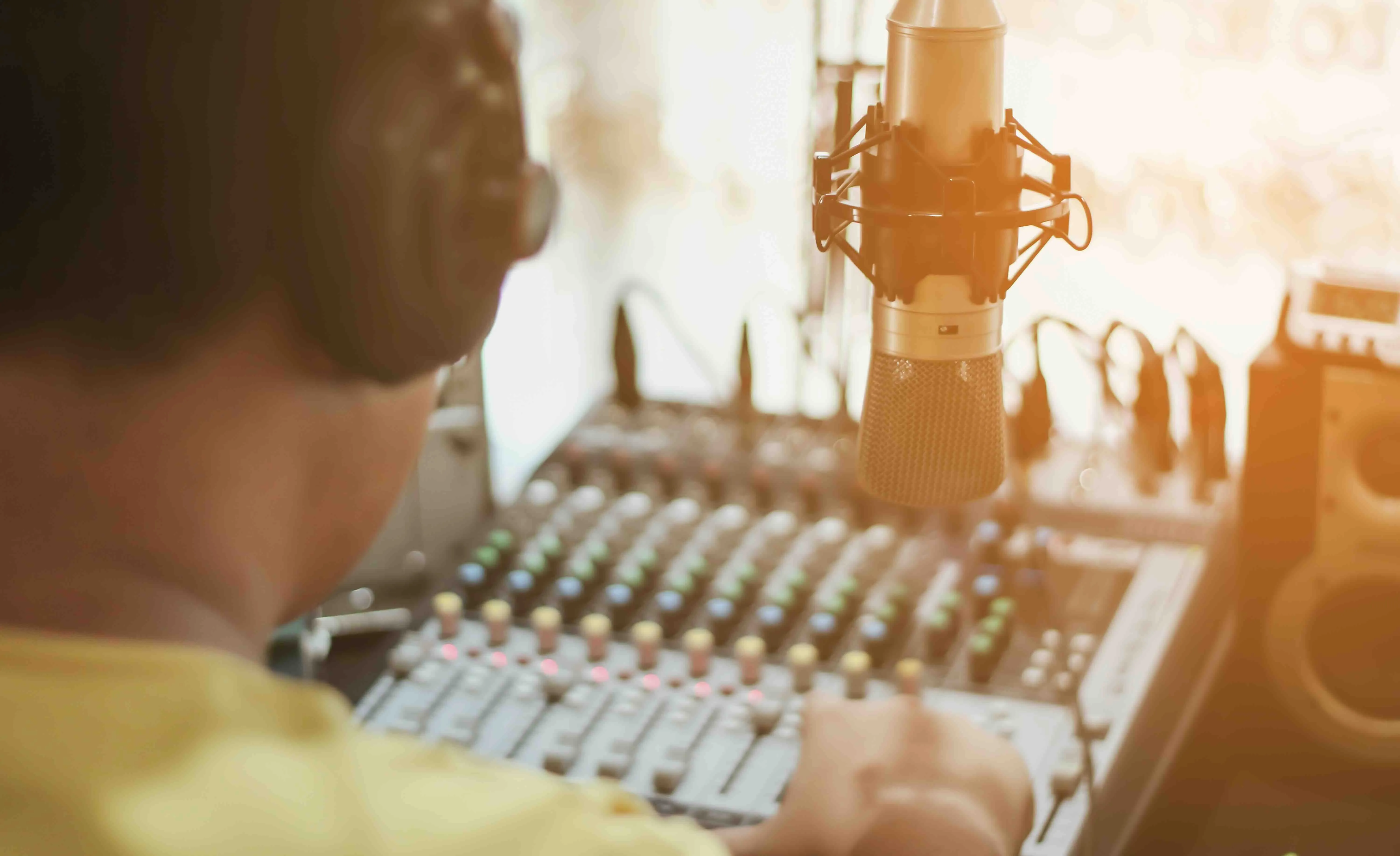 Leitender Toningenieur mit Kopfhörern an einem Mischpult im Tonstudio vor einem aufgehängten Mikrofon.