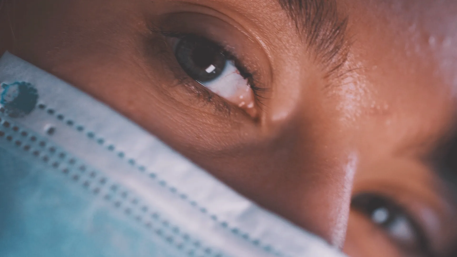 Nahaufnahme einer Person mit blauen Augen, die eine blaue medizinische Maske trägt.