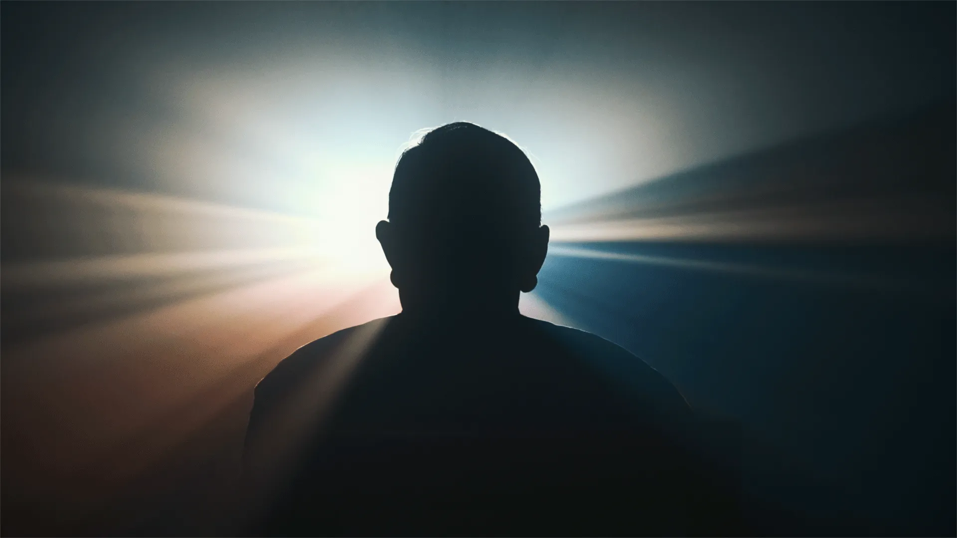 Silhouette einer Person vor einem hellen Licht mit strahlenförmigen Lichtstrahlen im Hintergrund.