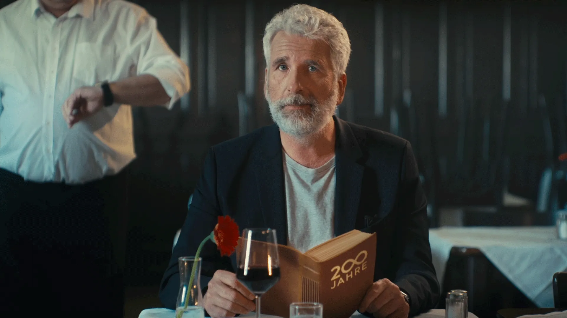 A man is sitting in a restaurant with a book and looking directly at the camera